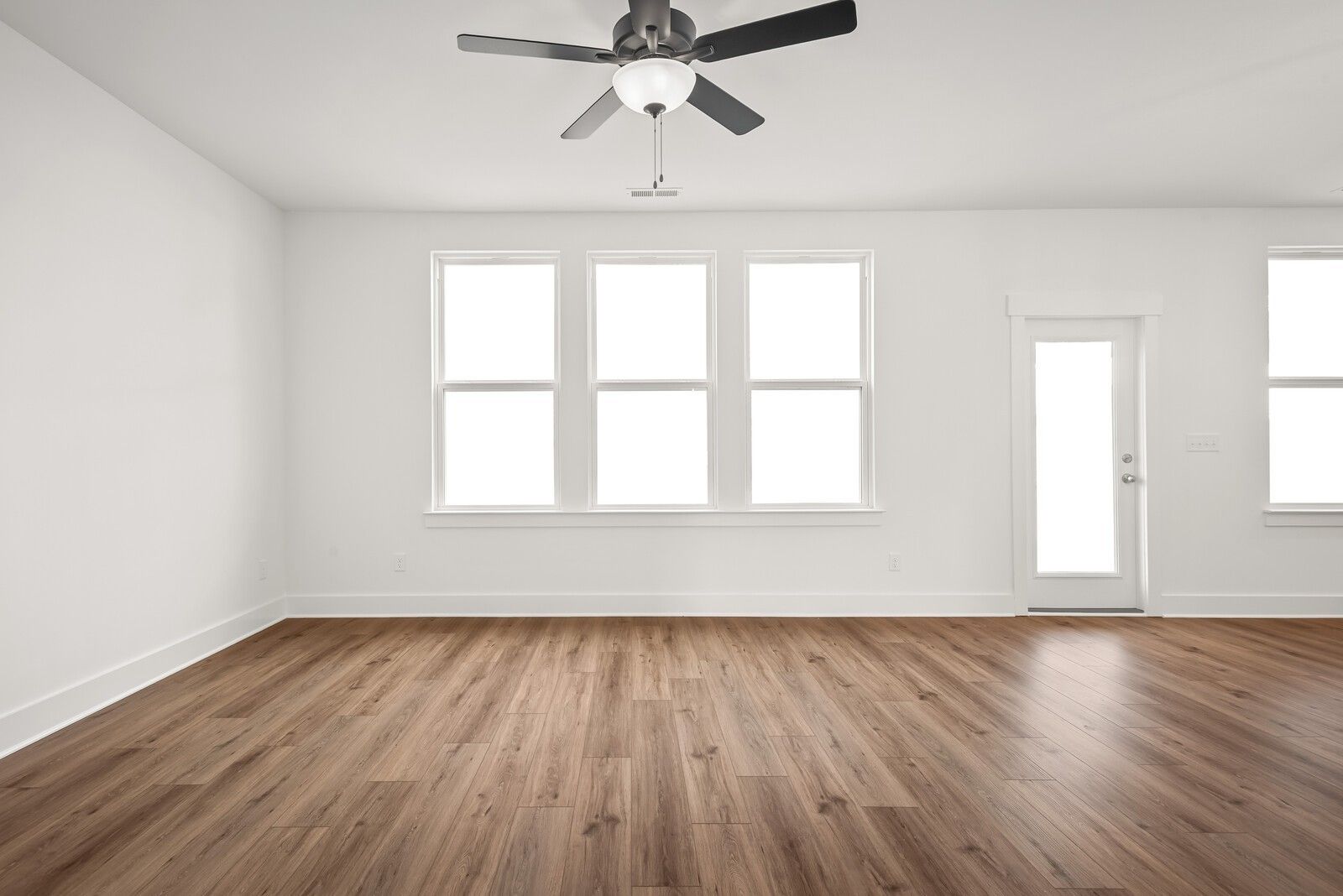 Bright empty living room with large windows, hardwood floors, and ceiling fan in Davidson Homes The Logan C, Gallatin, TN
