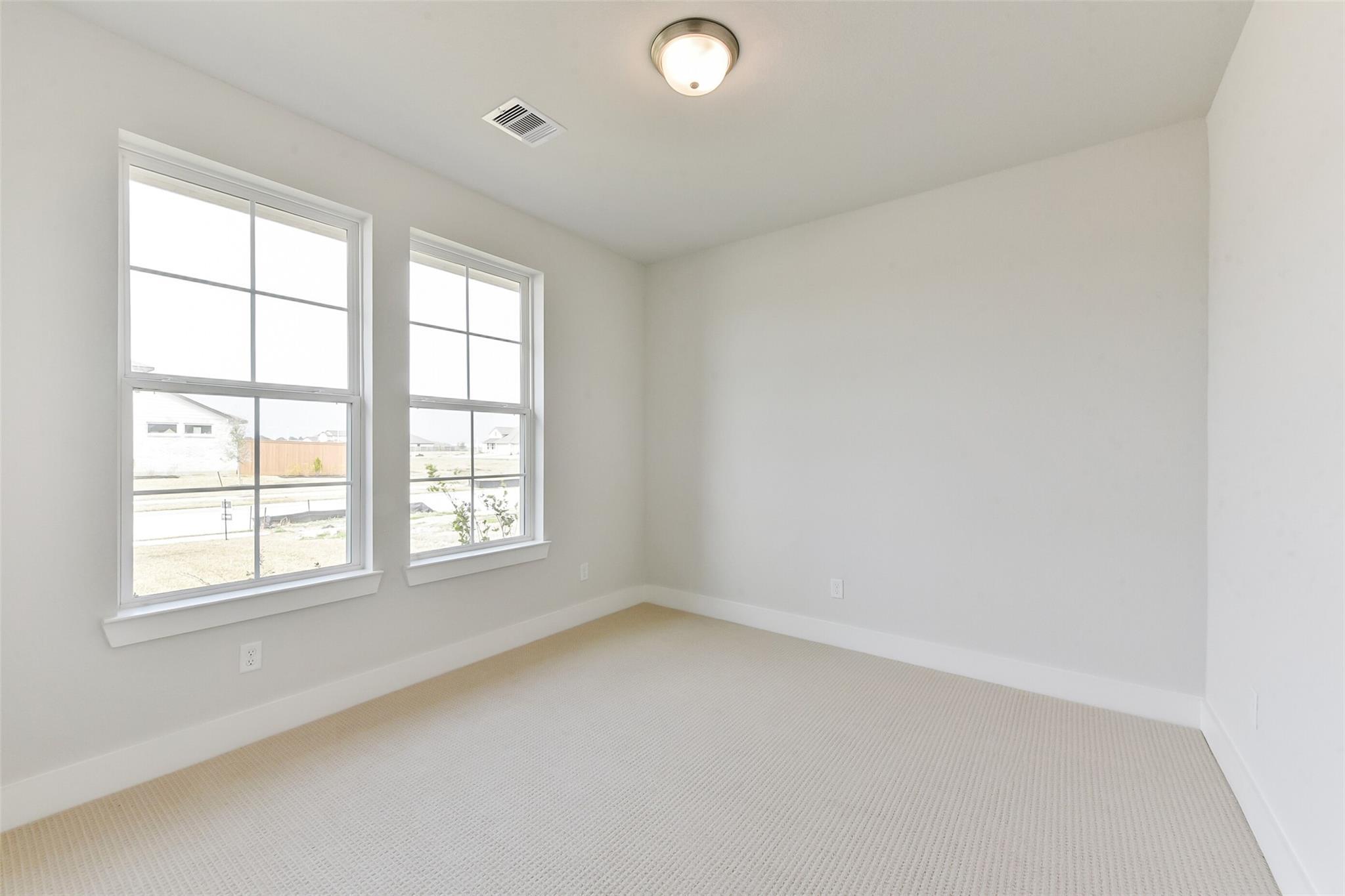 Bright empty bedroom with large windows, neutral carpet, and modern lighting in Davidson Homes Edward A, Lago Mar, Texas City