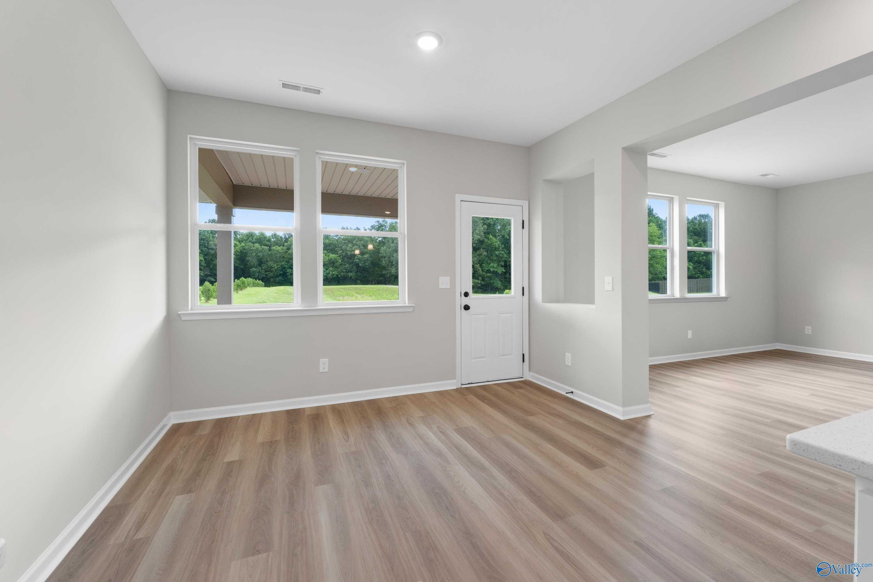 Bright open living room with light gray walls, large windows overlooking lush greenery, white entry door, and hardwood floors in Davidson Homes The Dorado, Huntsville AL