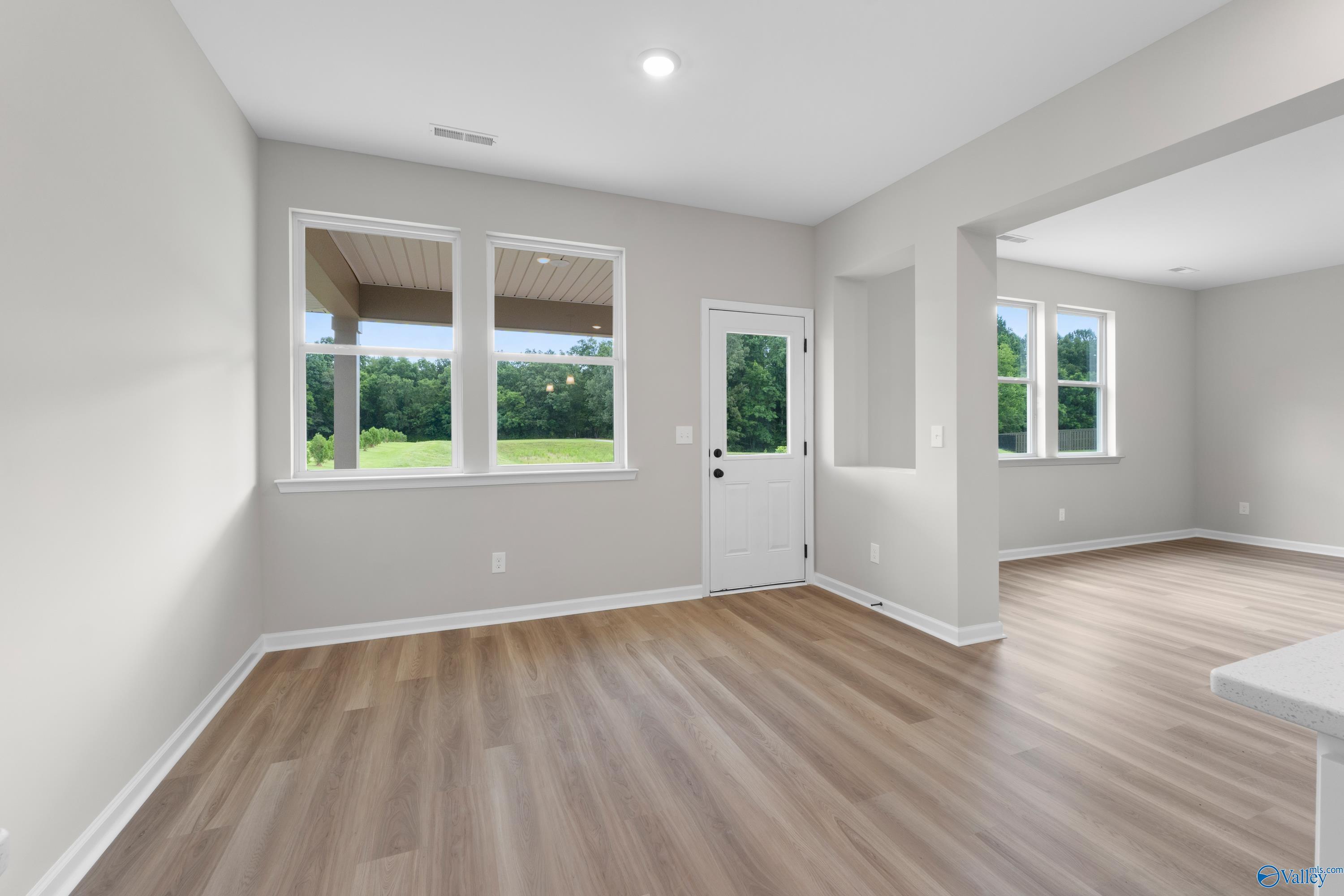 Bright open living room with light gray walls, large windows overlooking lush greenery, white entry door, and hardwood floors in Davidson Homes The Dorado, Huntsville AL