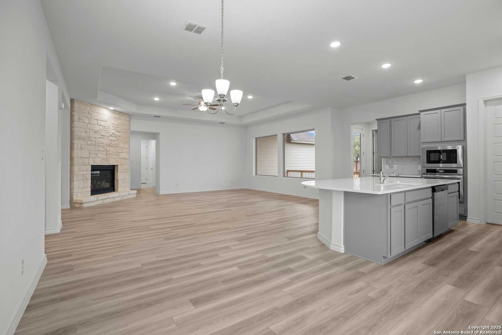 Open-concept living room with stone fireplace, gray kitchen island, and recessed lighting in The Summerlin B, Castroville, Texas