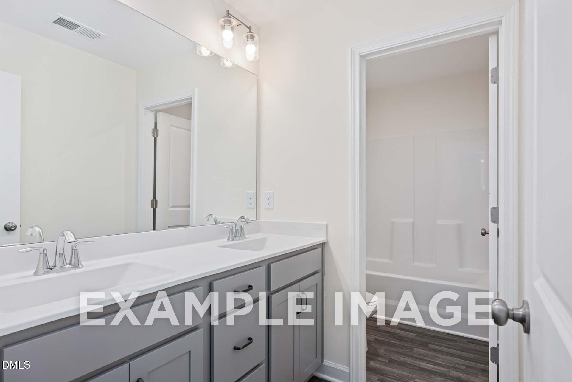 Modern master bathroom with double vanity, gray cabinets, large mirror, and adjacent shower in The Ash B by Davidson Homes, Zebulon, NC