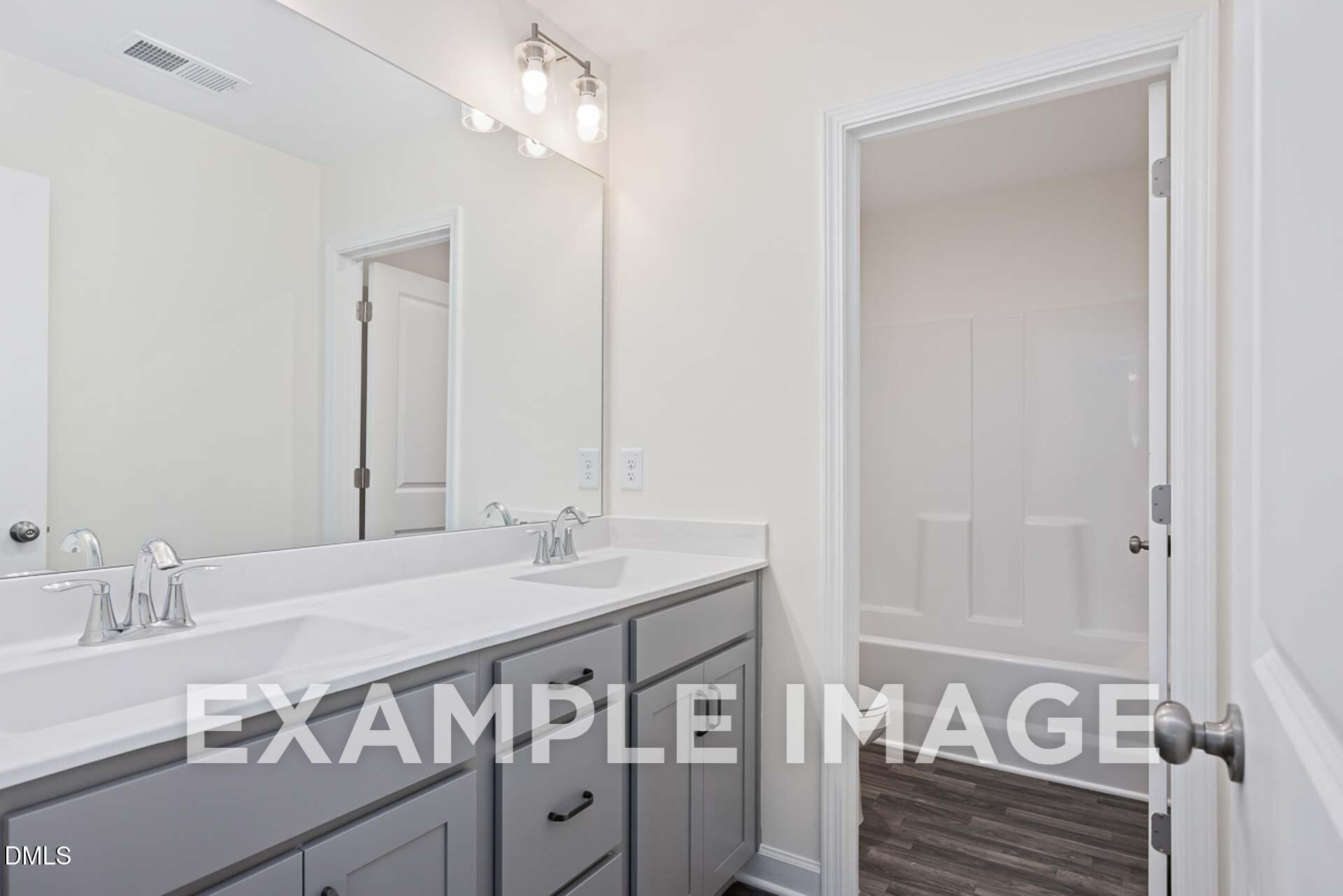 Elegant master bath with double vanity, soaking tub, and wood flooring in The Ash B by Davidson Homes, Zebulon, NC
