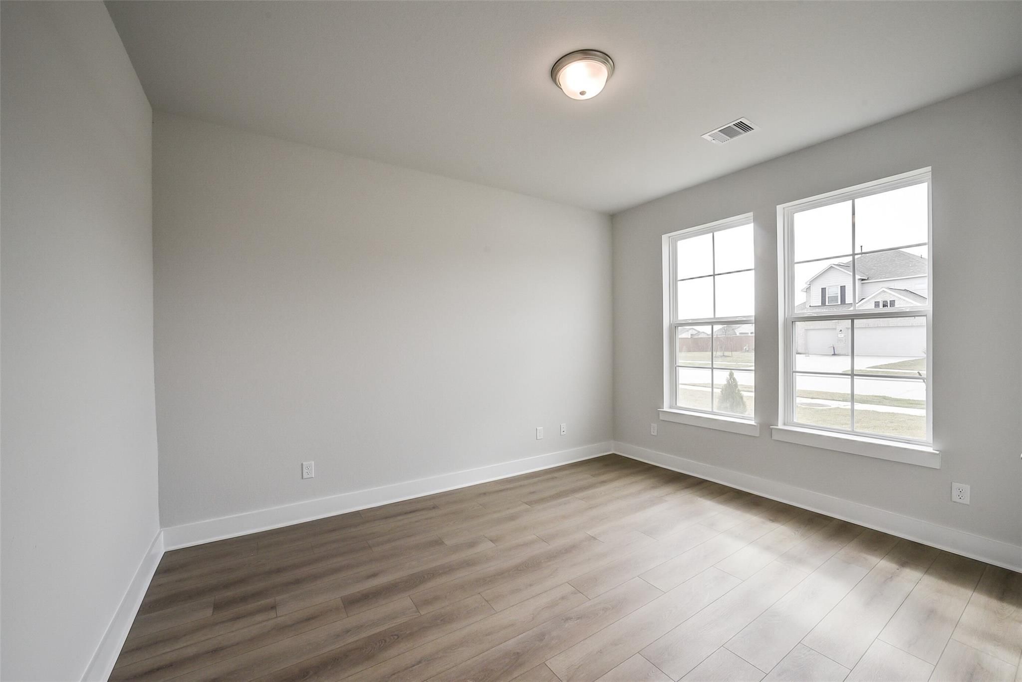 Bright secondary bedroom with light gray walls, laminate wood floors, and double windows in Davidson Homes The Philip B, Rosharon, Texas