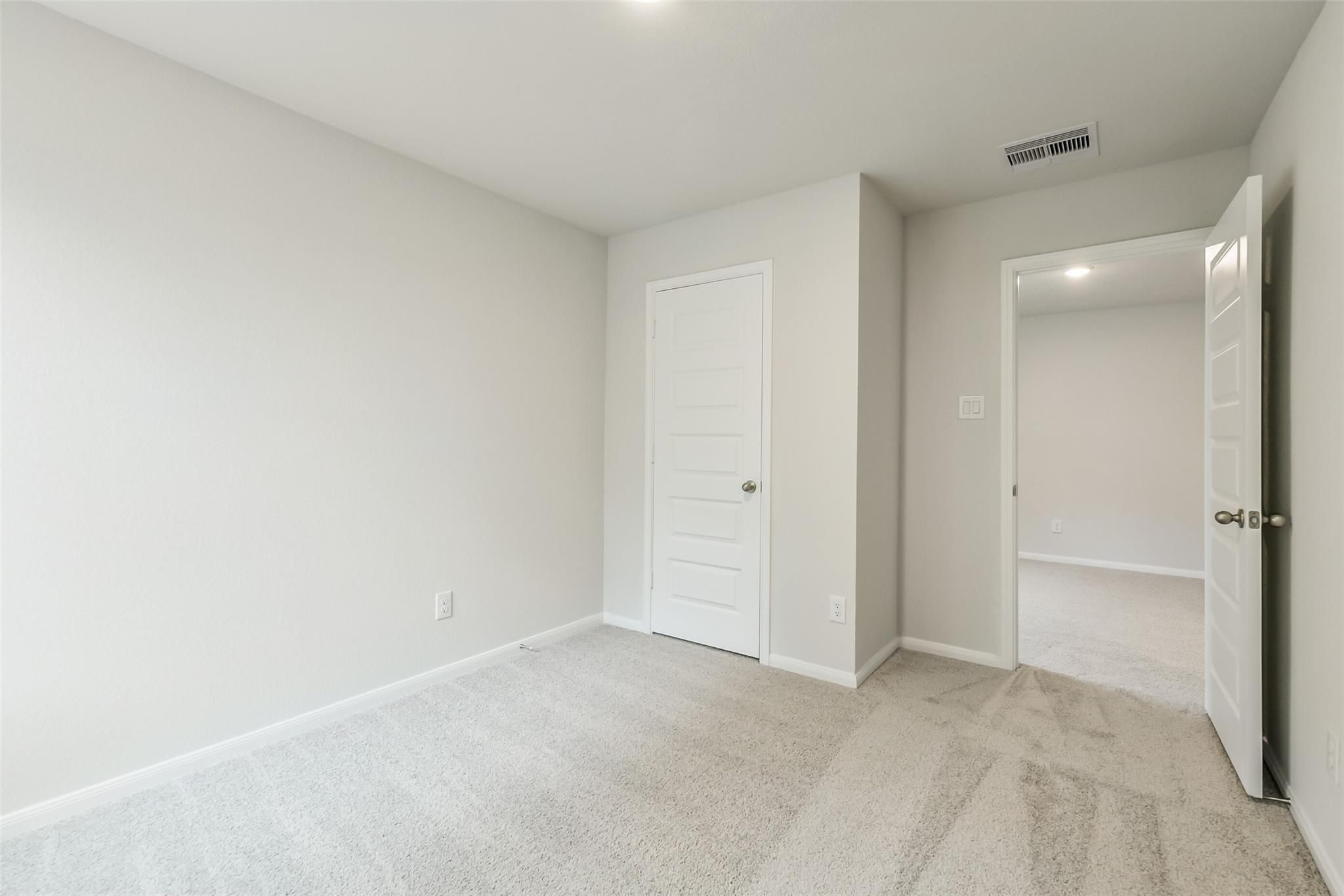 Bright secondary bedroom featuring neutral walls, carpeted floors, and open bath door in Davidson Homes The Brazos F, Conroe, Texas