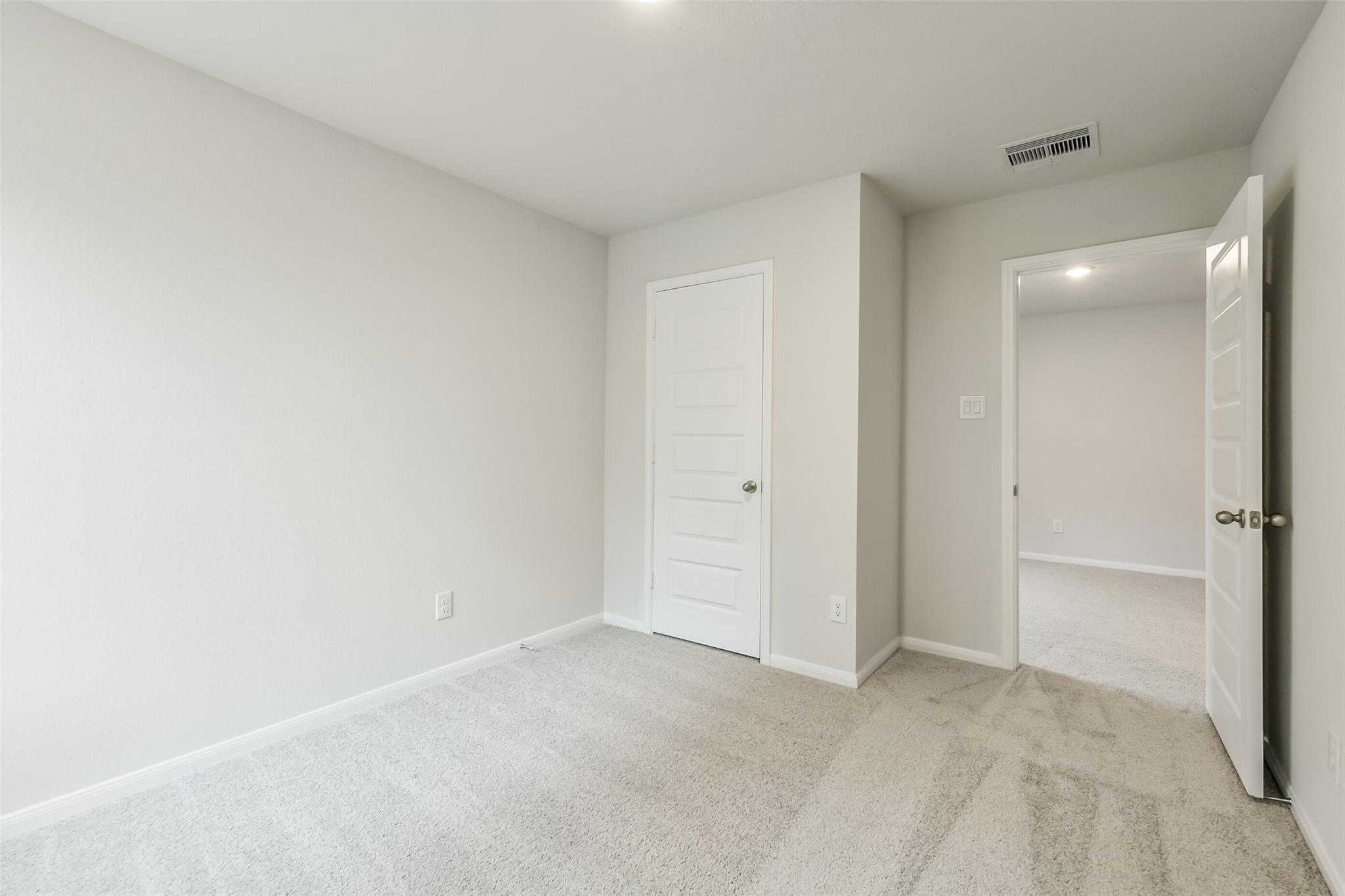 Bright secondary bedroom featuring neutral walls, carpeted floors, and open bath door in Davidson Homes The Brazos F, Conroe, Texas
