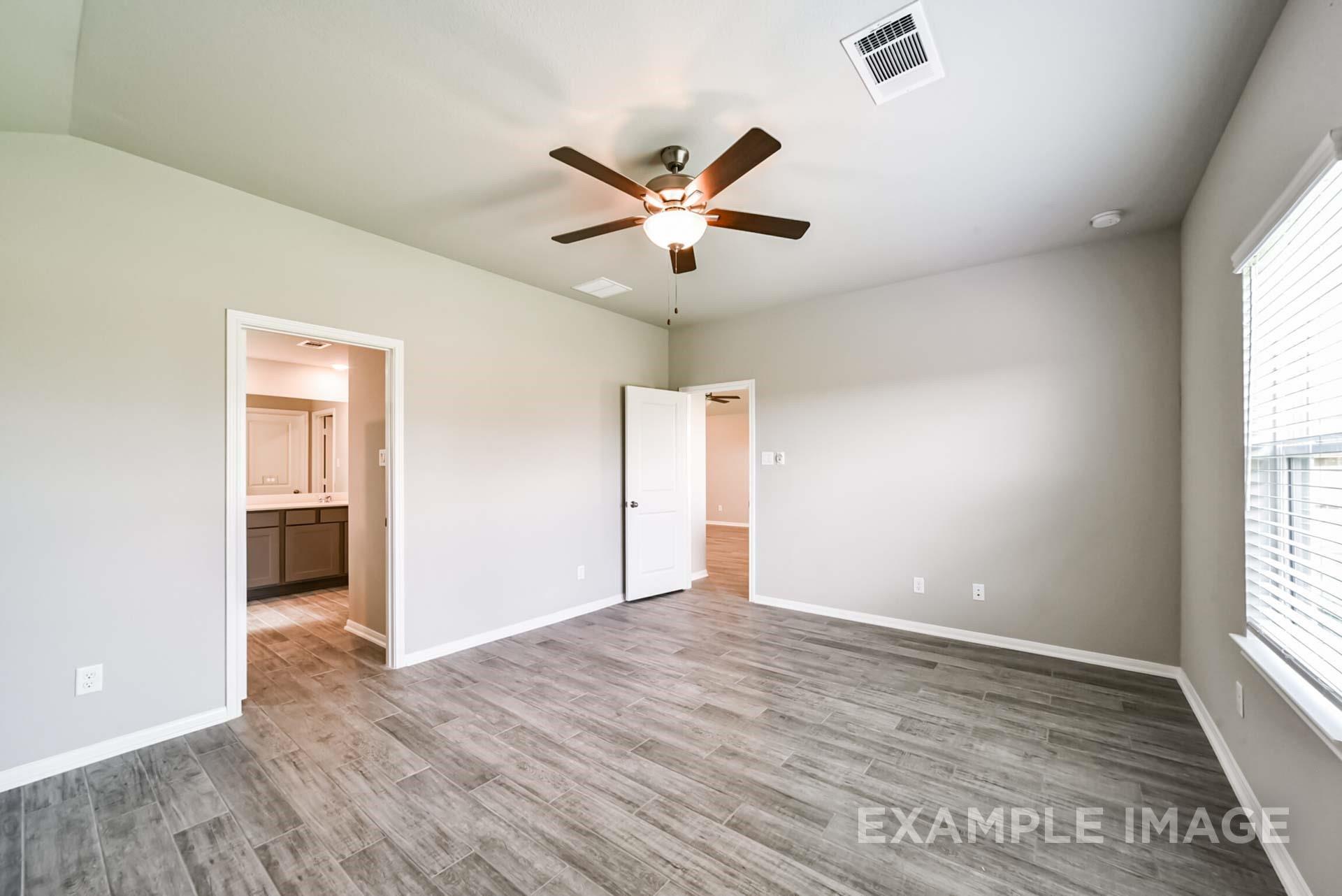 Spacious bedroom with wood-look tile floors and ceiling fan in The Riviera A floor plan at Emberly in Beasley, Texas.