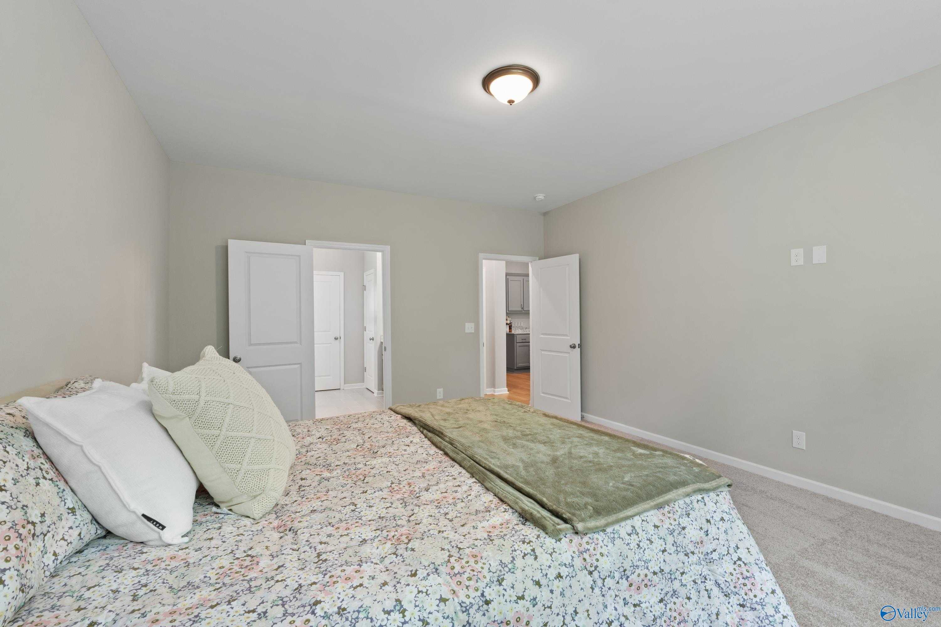 Cozy bedroom with floral bedding, green throw, and adjacent bathroom in Davidson Homes The Luna, Hazel Green, Alabama