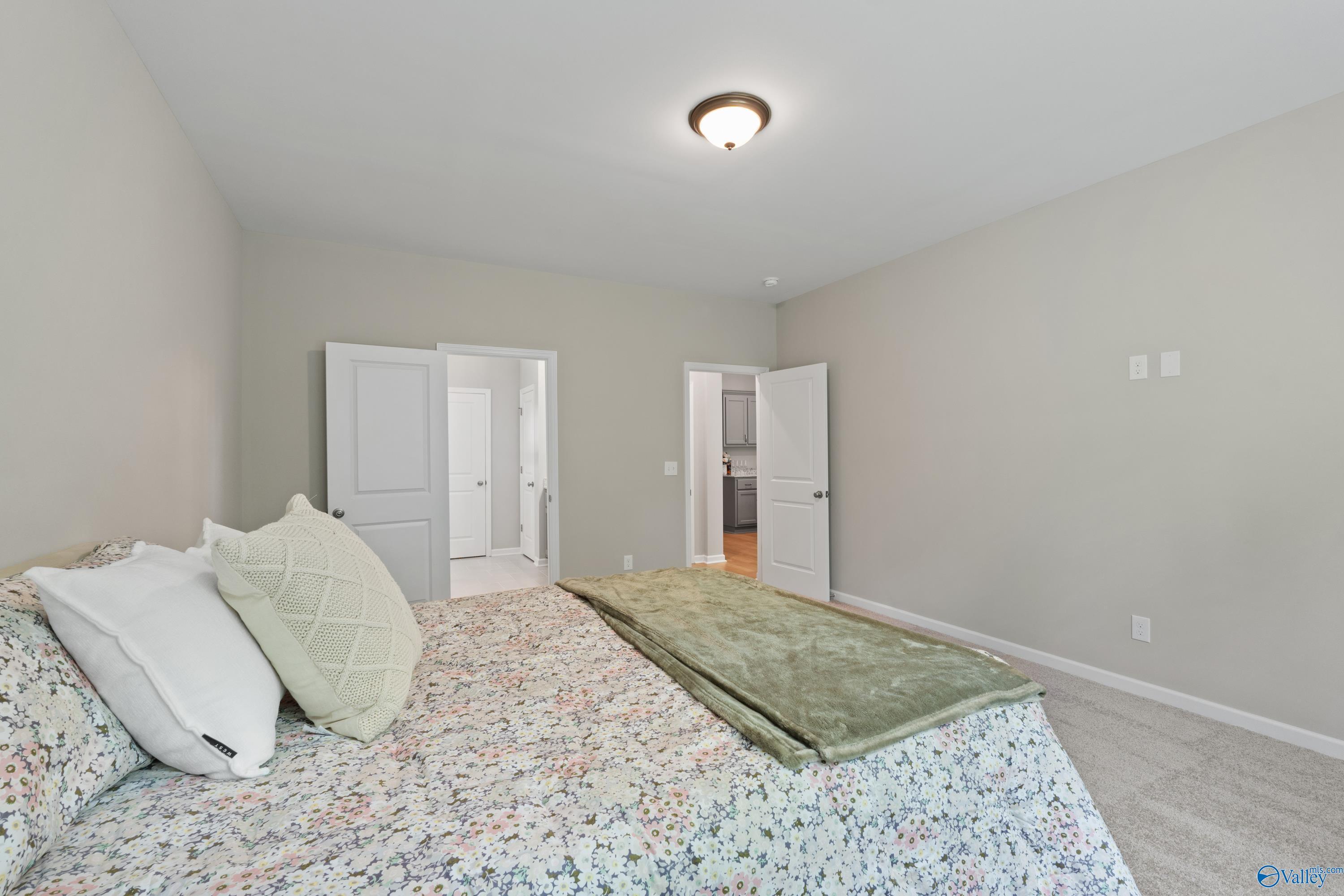 Cozy bedroom with floral comforter, green throw blanket, and open bathroom door in Davidson Homes The Luna, Hazel Green, Alabama
