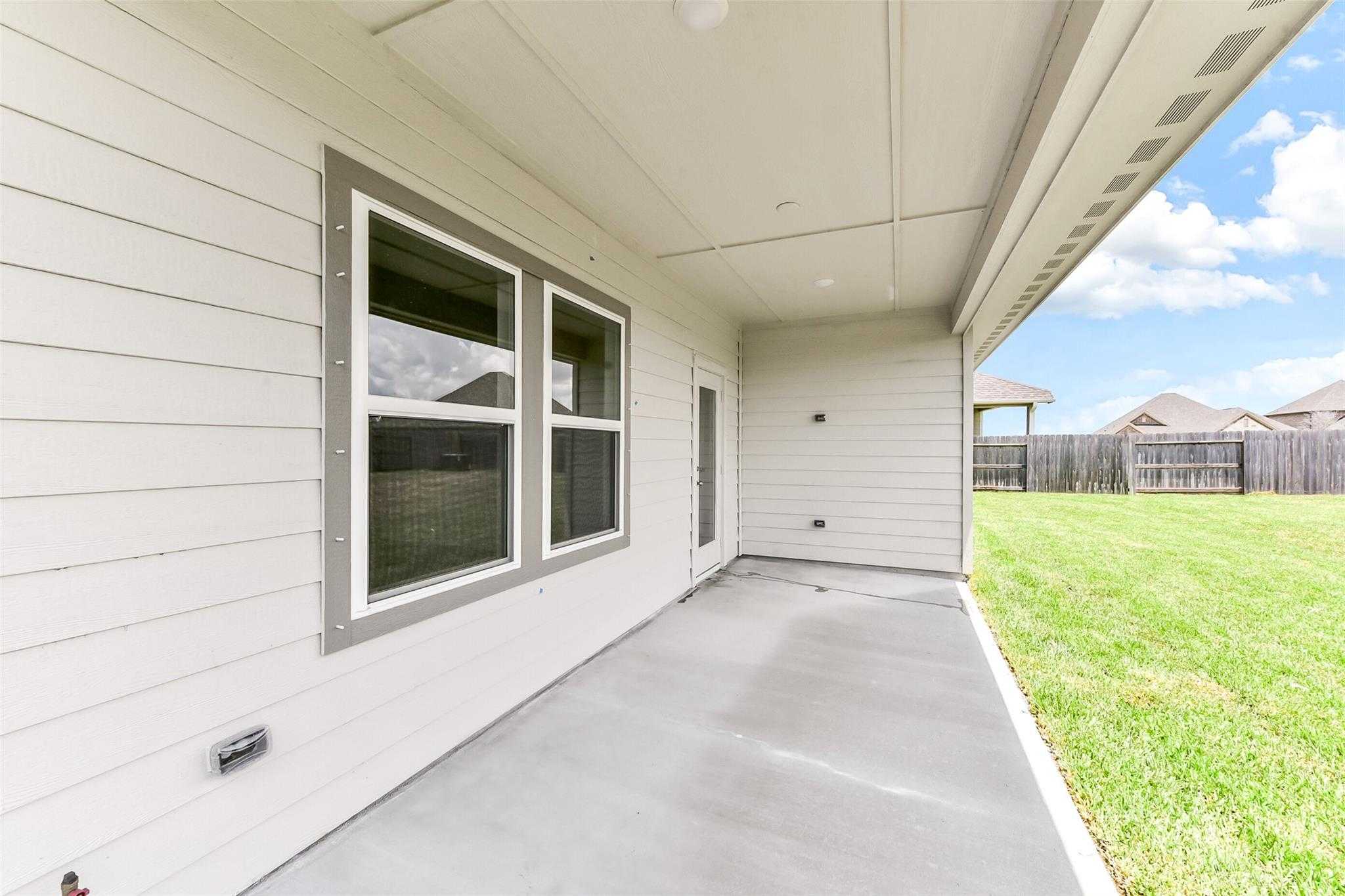 Covered back patio with concrete slab, large windows, and lush green lawn in Davidson Homes The Laguna C, Sierra Vista, Rosharon, Texas