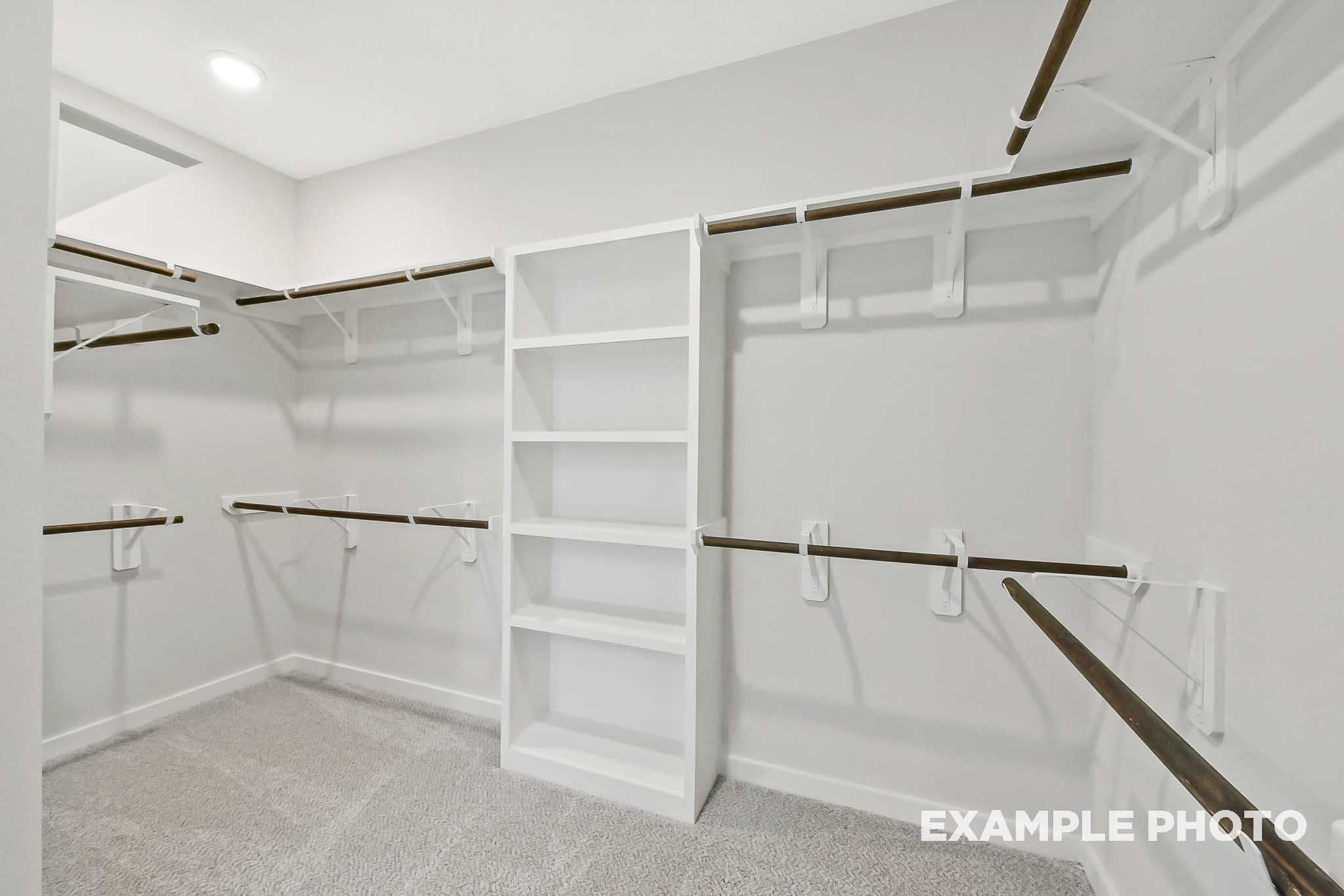 Spacious walk-in closet in The Sequoia master suite featuring white shelving, wooden rods, gray carpet, and neutral walls
