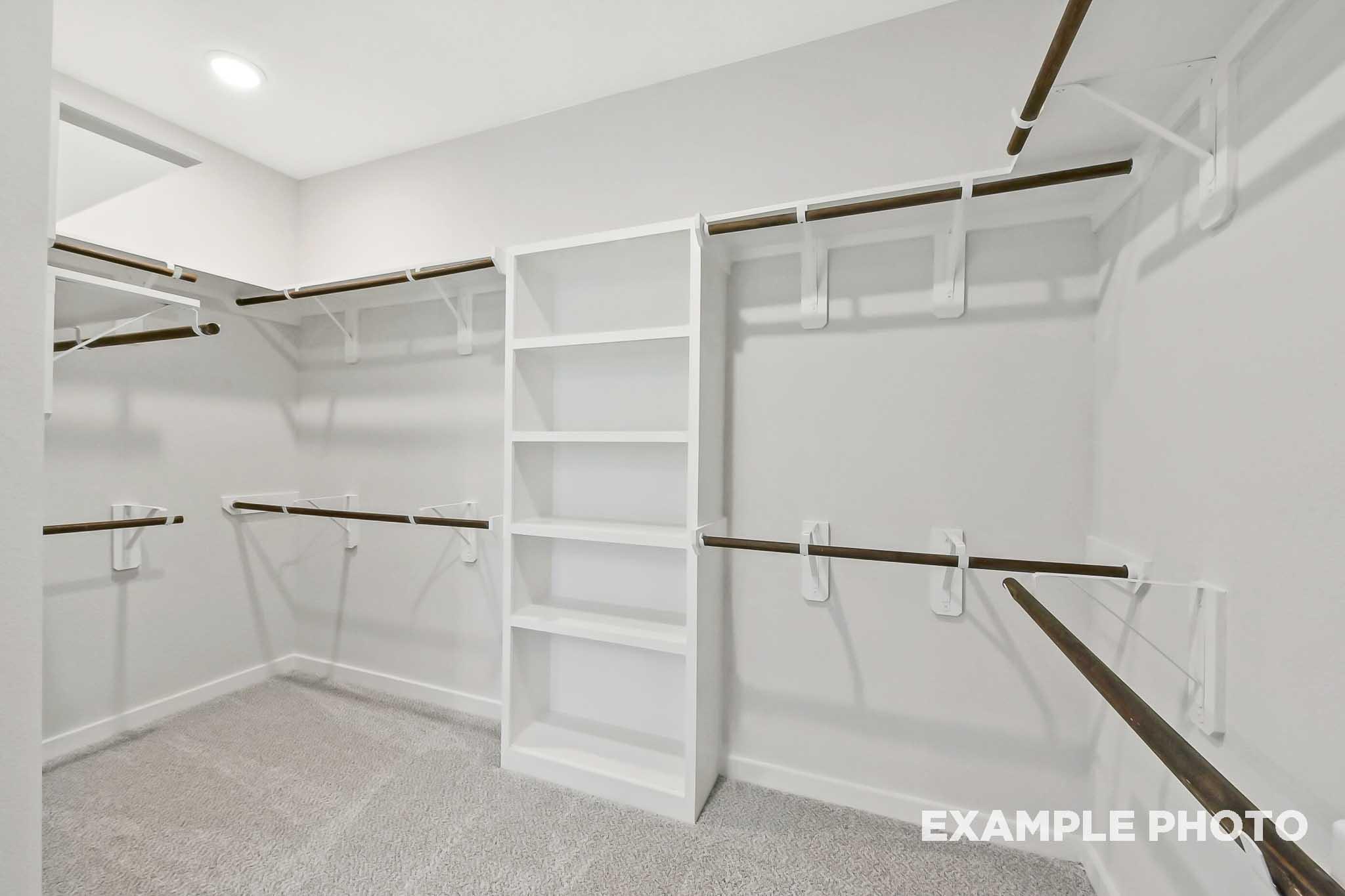 Spacious walk-in closet in The Sequoia master suite featuring white shelving, wooden rods, gray carpet, and neutral walls