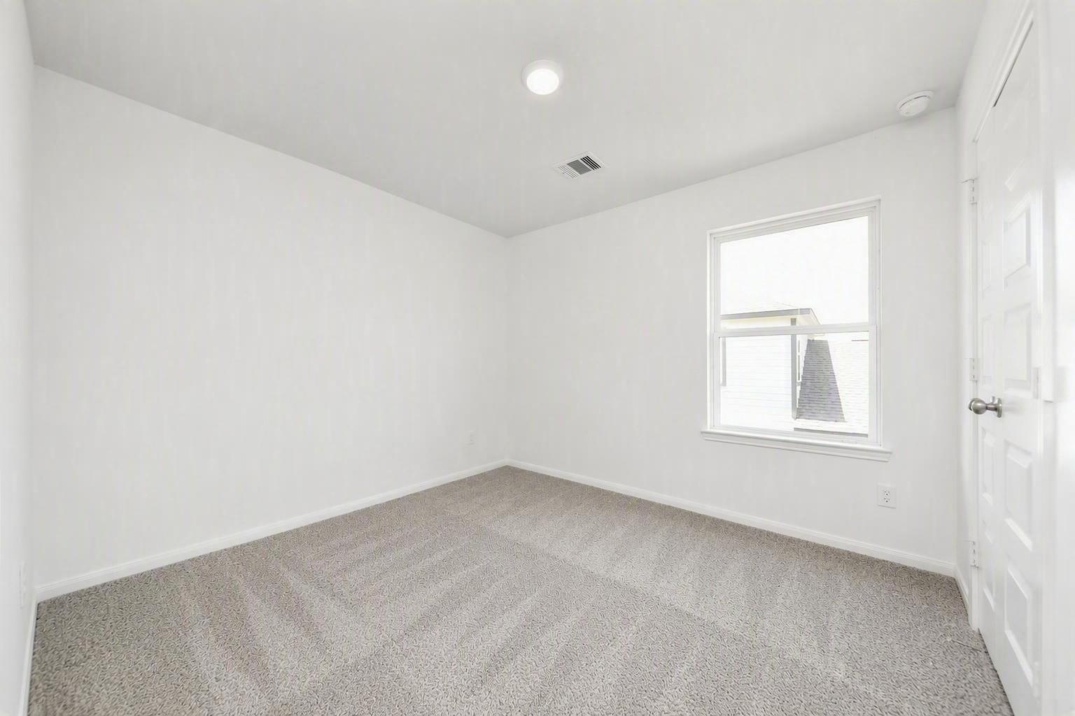 Bright empty bedroom with white walls, carpet flooring, and window in Davidson Homes Trinity F plan, Splendora, Texas