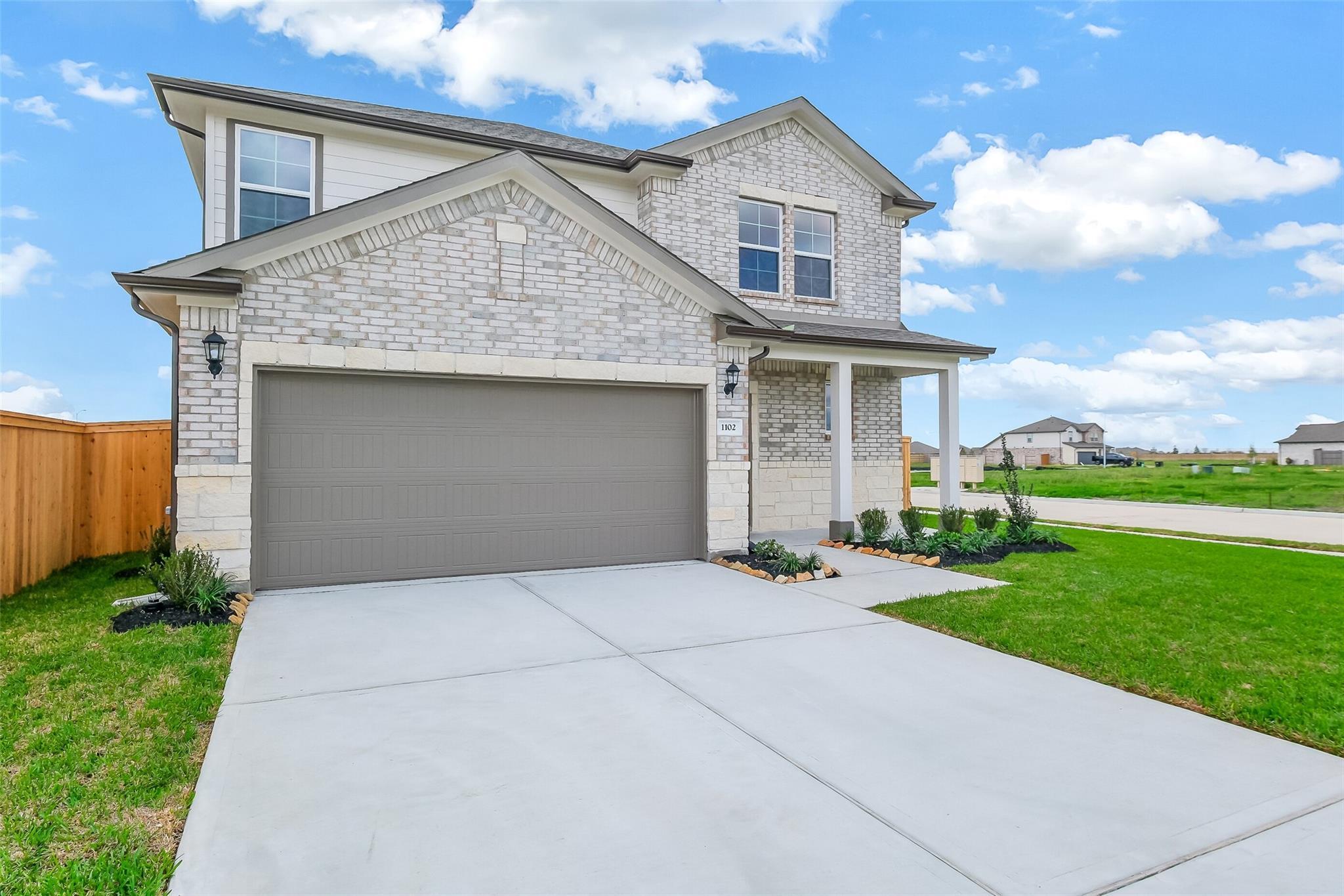 Two-story light brick home with two-car garage, driveway, and landscaped yard in Emberly, Beasley, Texas - Davidson Homes Tierra B