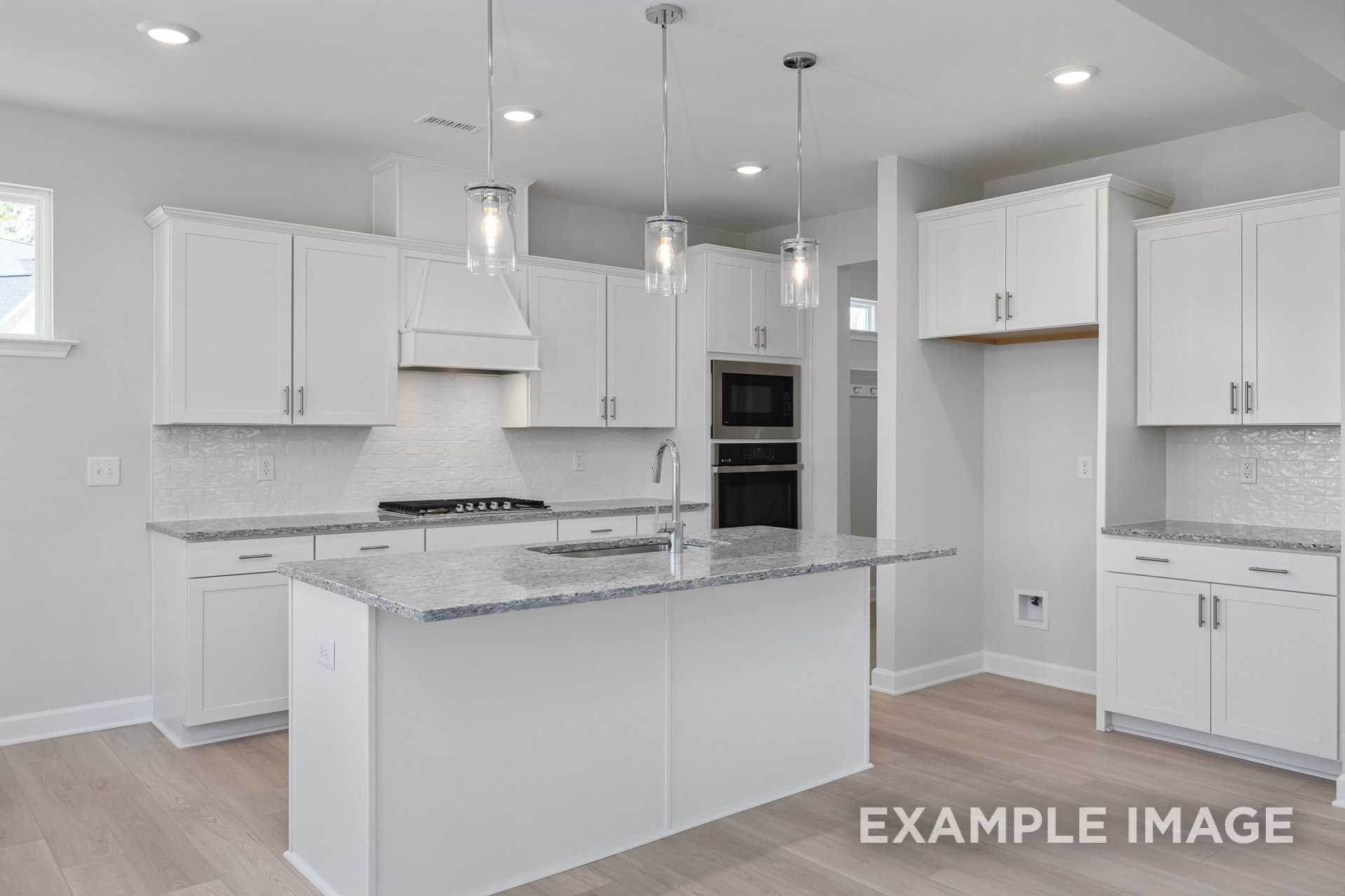 Spacious modern kitchen in The Gavin C home with white shaker cabinets, quartz island, double ovens, gas range, and pendant lights
