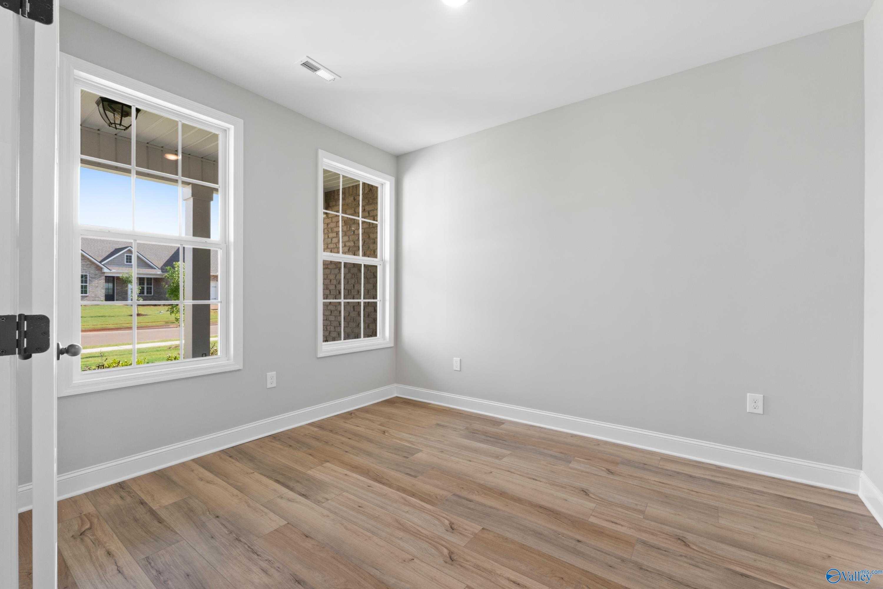 Bright secondary bedroom with gray walls, hardwood floors, and large windows overlooking lawn in Davidson Homes The Rockford, Toney, Alabama