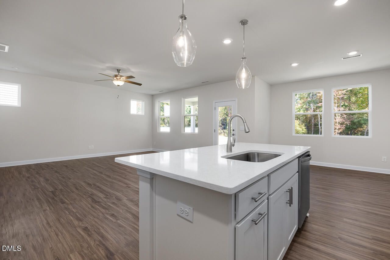 Modern open-concept kitchen with white quartz island, sink, pendant lights, and hardwood floors in The Grace C, Lillington, NC