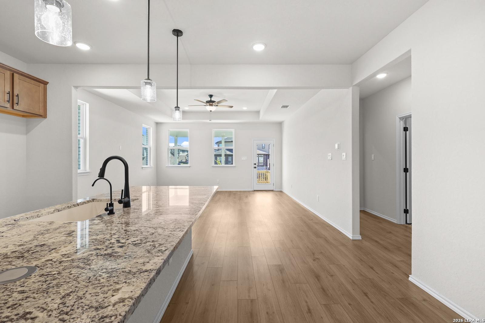 Open-concept kitchen and living area with granite island, pendant lights, and hardwood floors in Davidson Homes Glenwood E, San Antonio