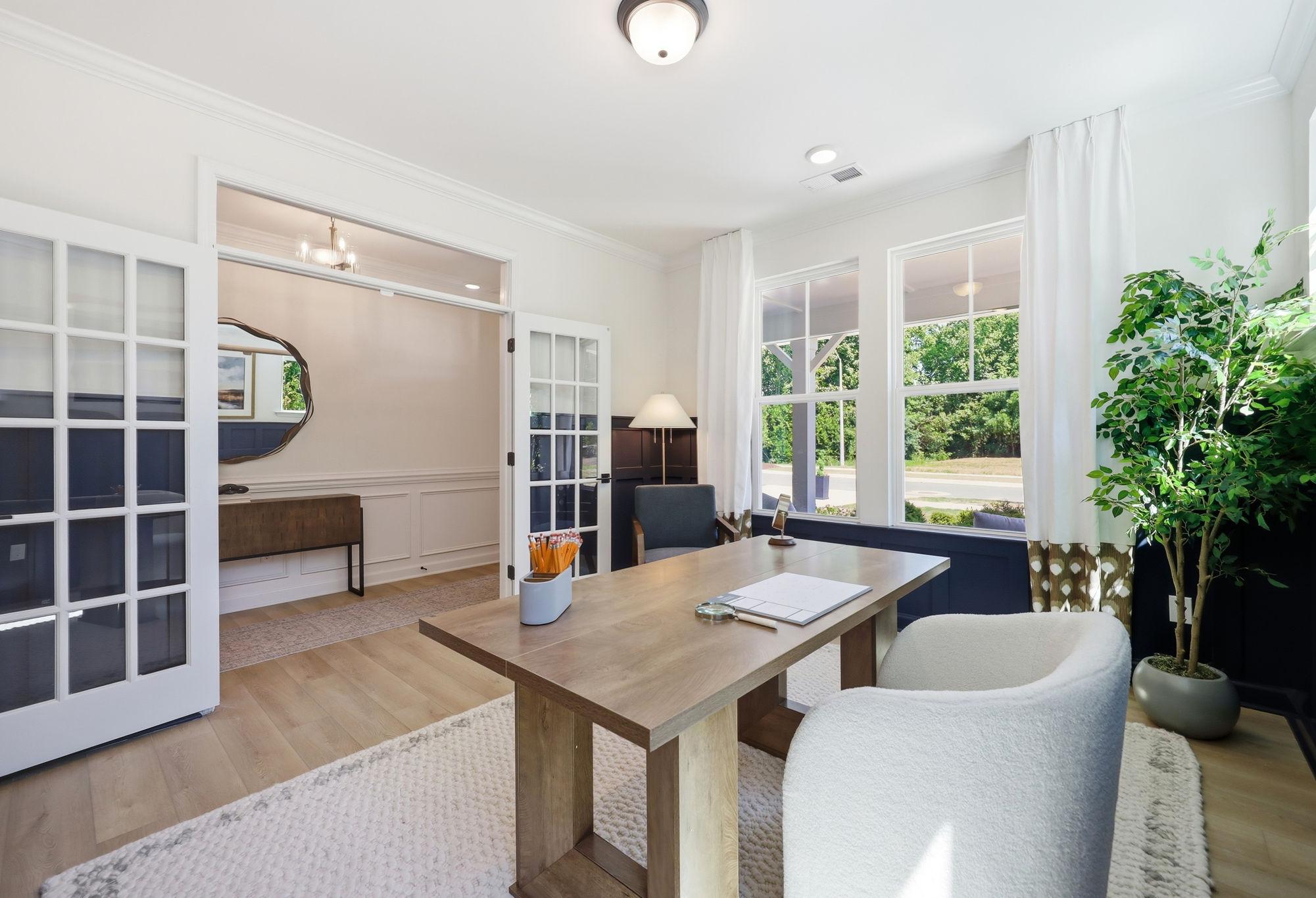 Bright home office in The Aspen by Davidson Homes featuring a wooden desk, French doors, and elegant interior design.