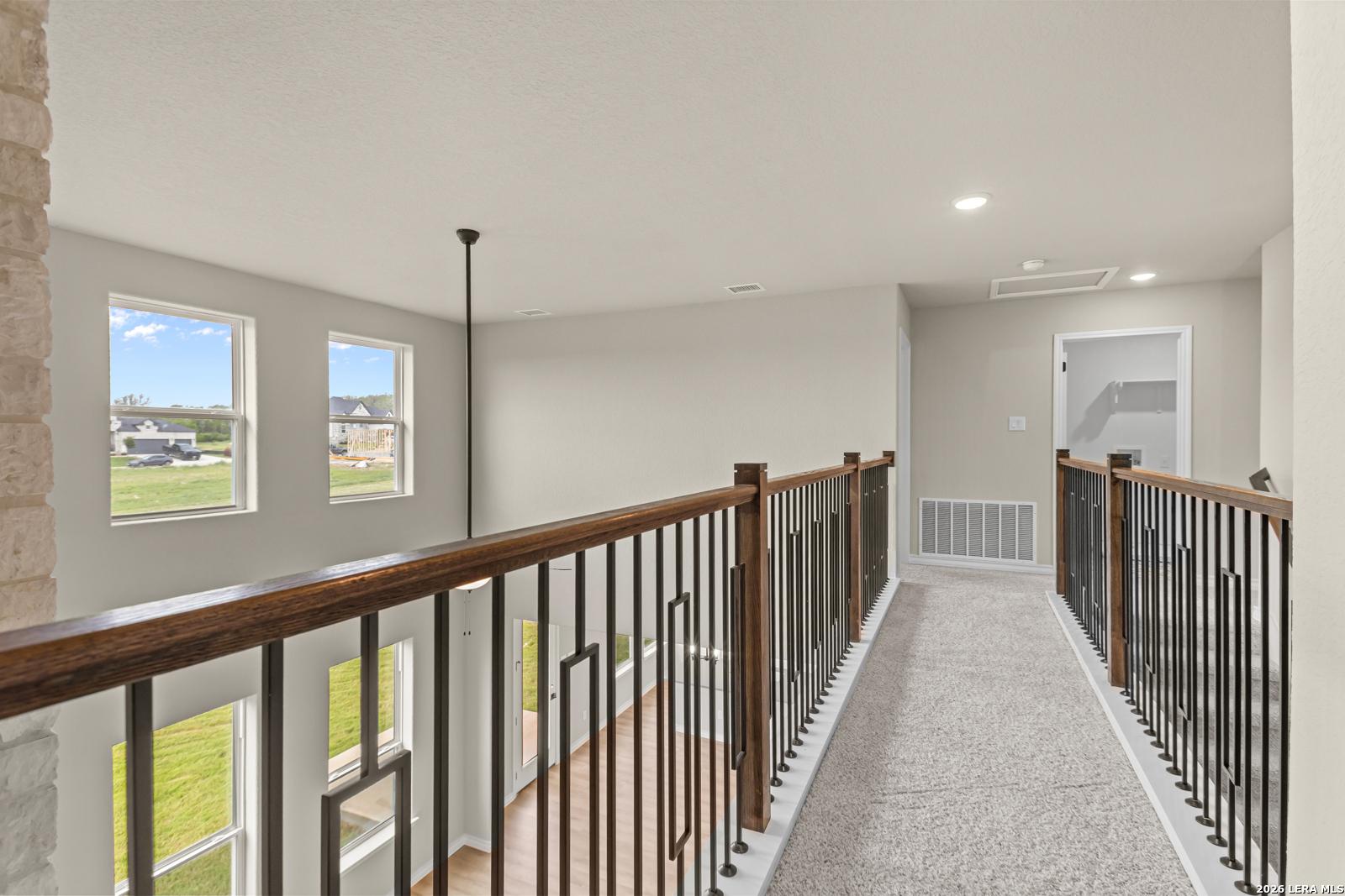 Second-floor carpeted walkway with elegant iron railing overlooking the main level in The Danbury H, Castroville, TX.