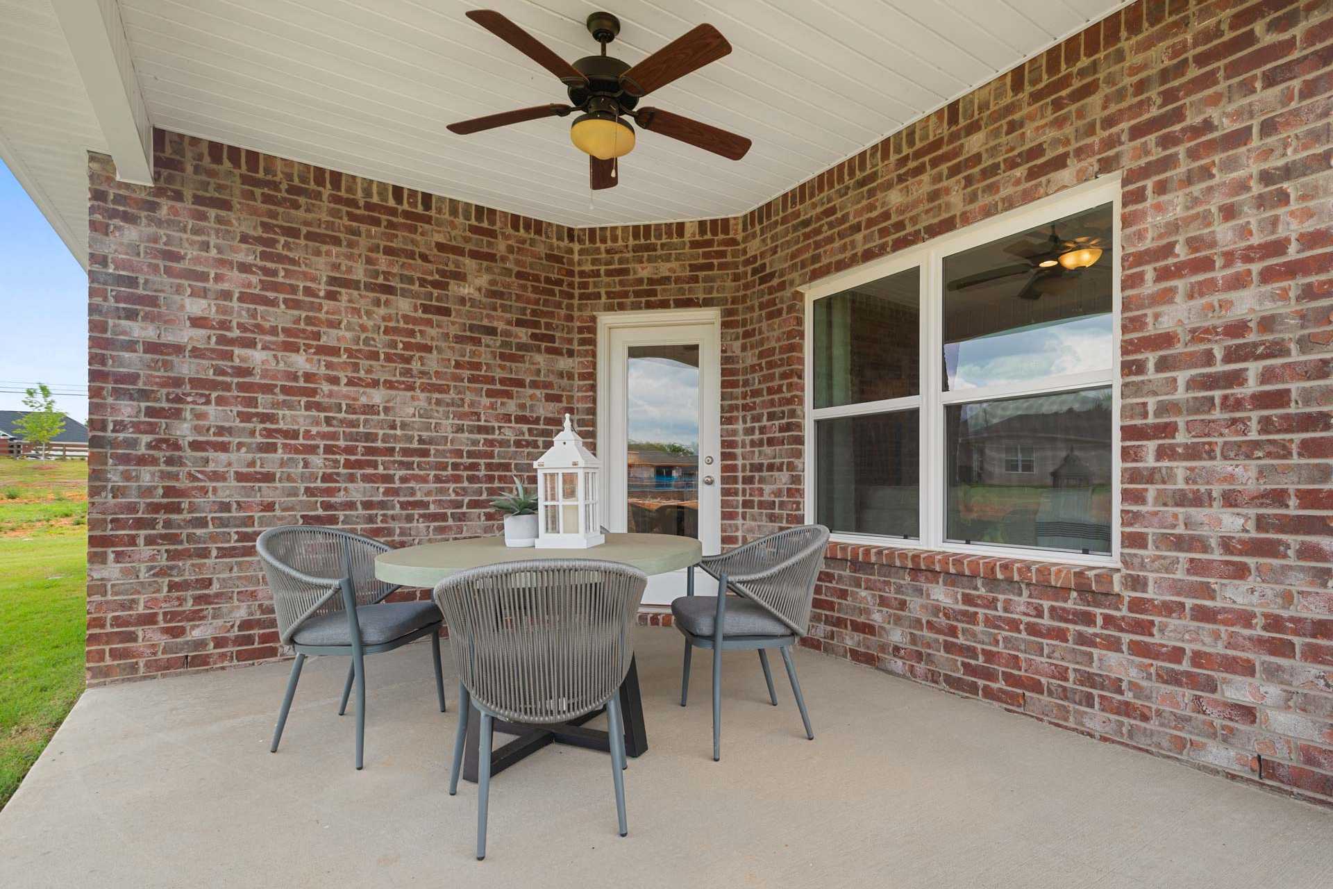 Covered brick patio at Flint Meadows in New Market Alabama with ceiling fan, round wicker table, chairs, and large windows