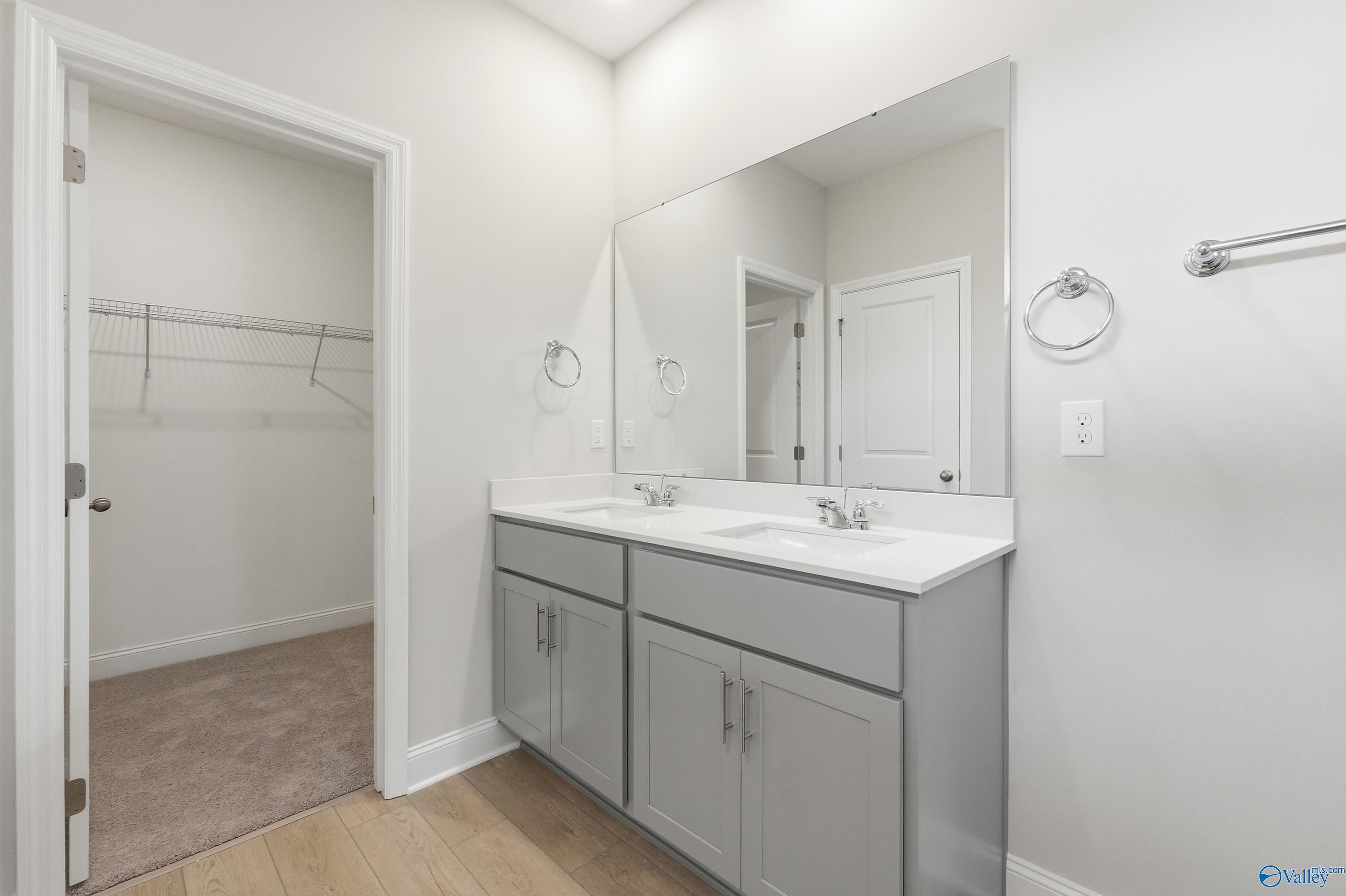 Modern master bathroom featuring double vanity with gray cabinets, large mirrors, and open walk-in closet in Davidson Homes The Franklin, Meridianville, Alabama