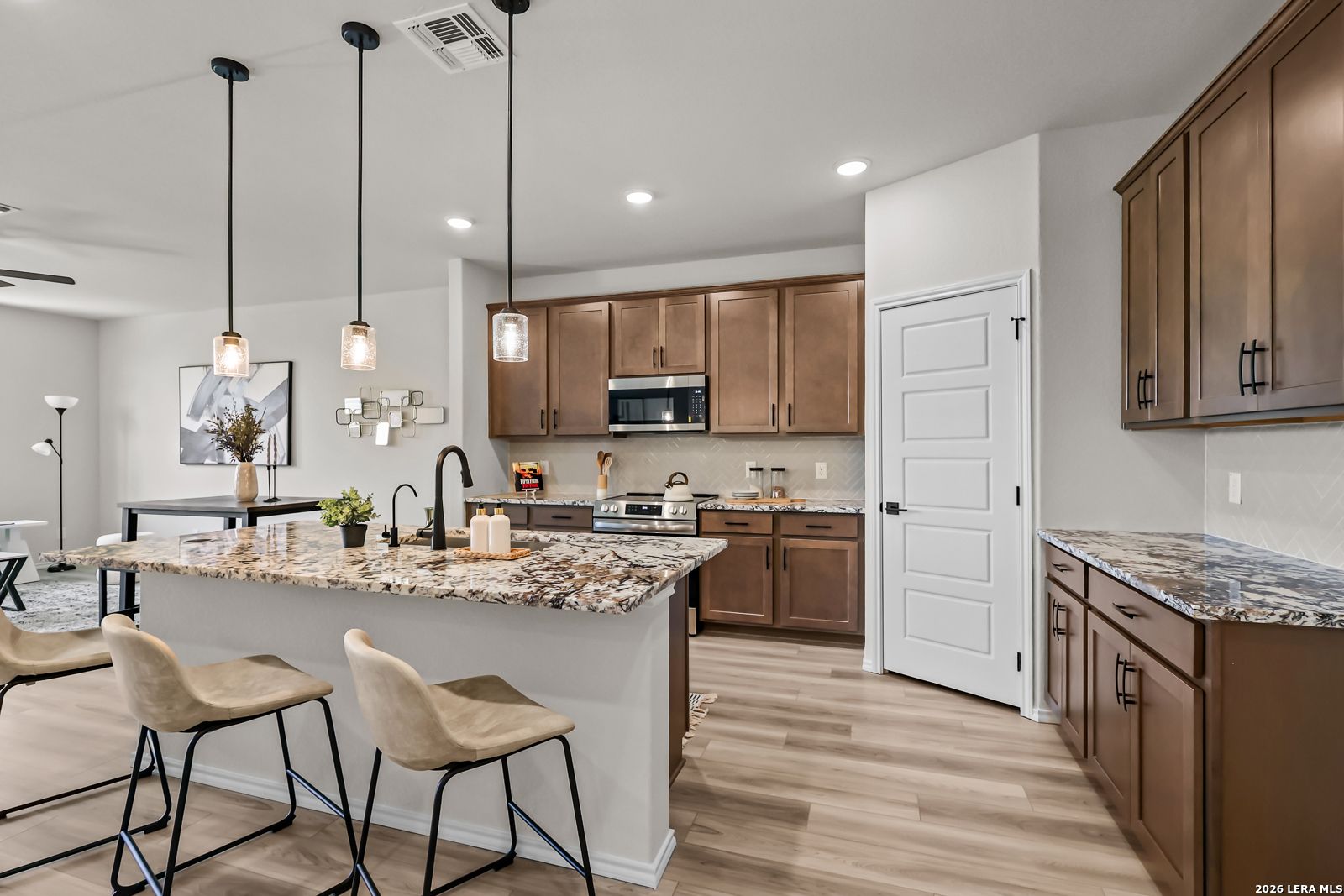 Modern kitchen with granite island, brown cabinets, and stainless appliances in The Douglas C floor plan, Seguin, Texas.