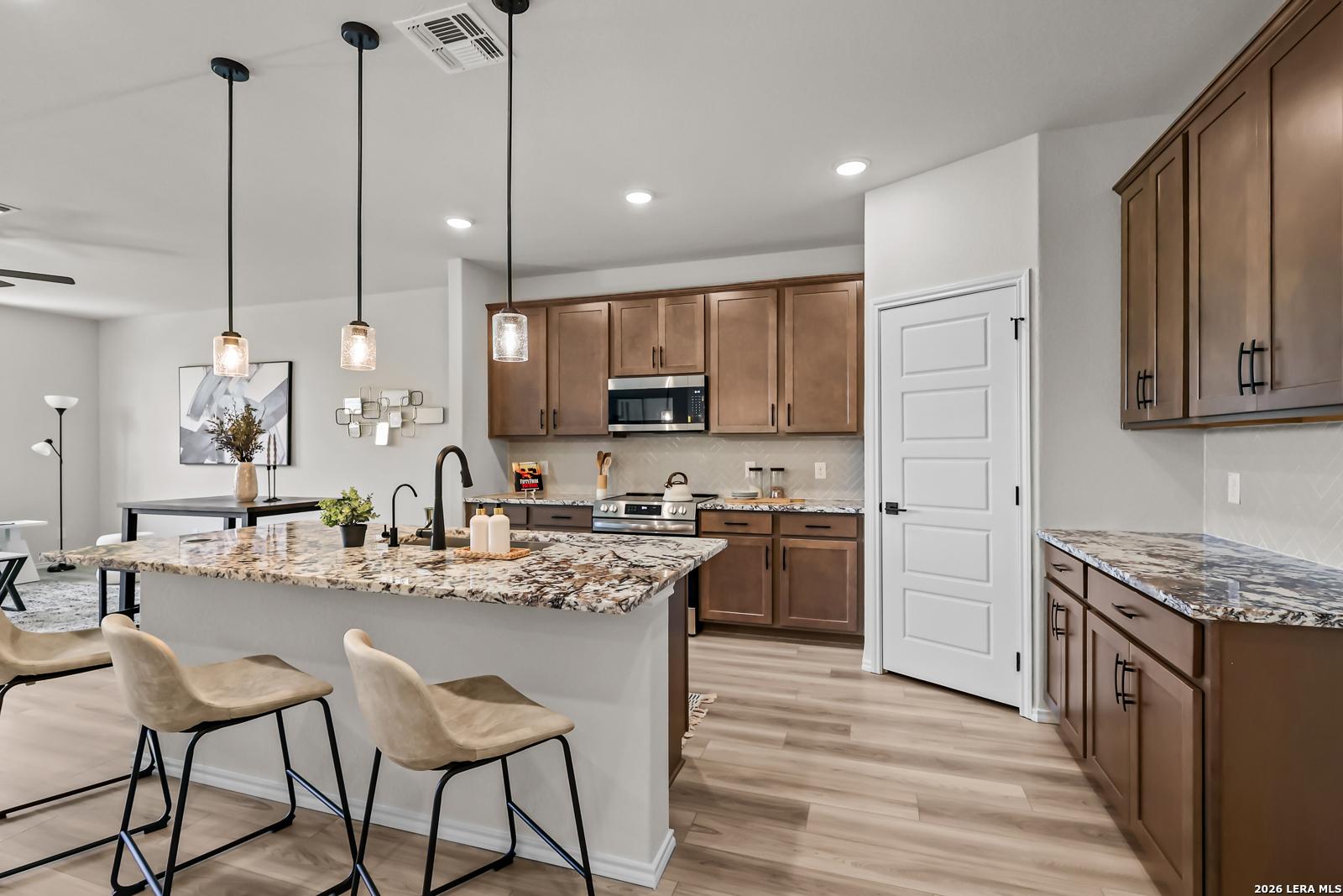 Modern kitchen with granite island, brown cabinets, and stainless appliances in The Douglas C floor plan, Seguin, Texas.