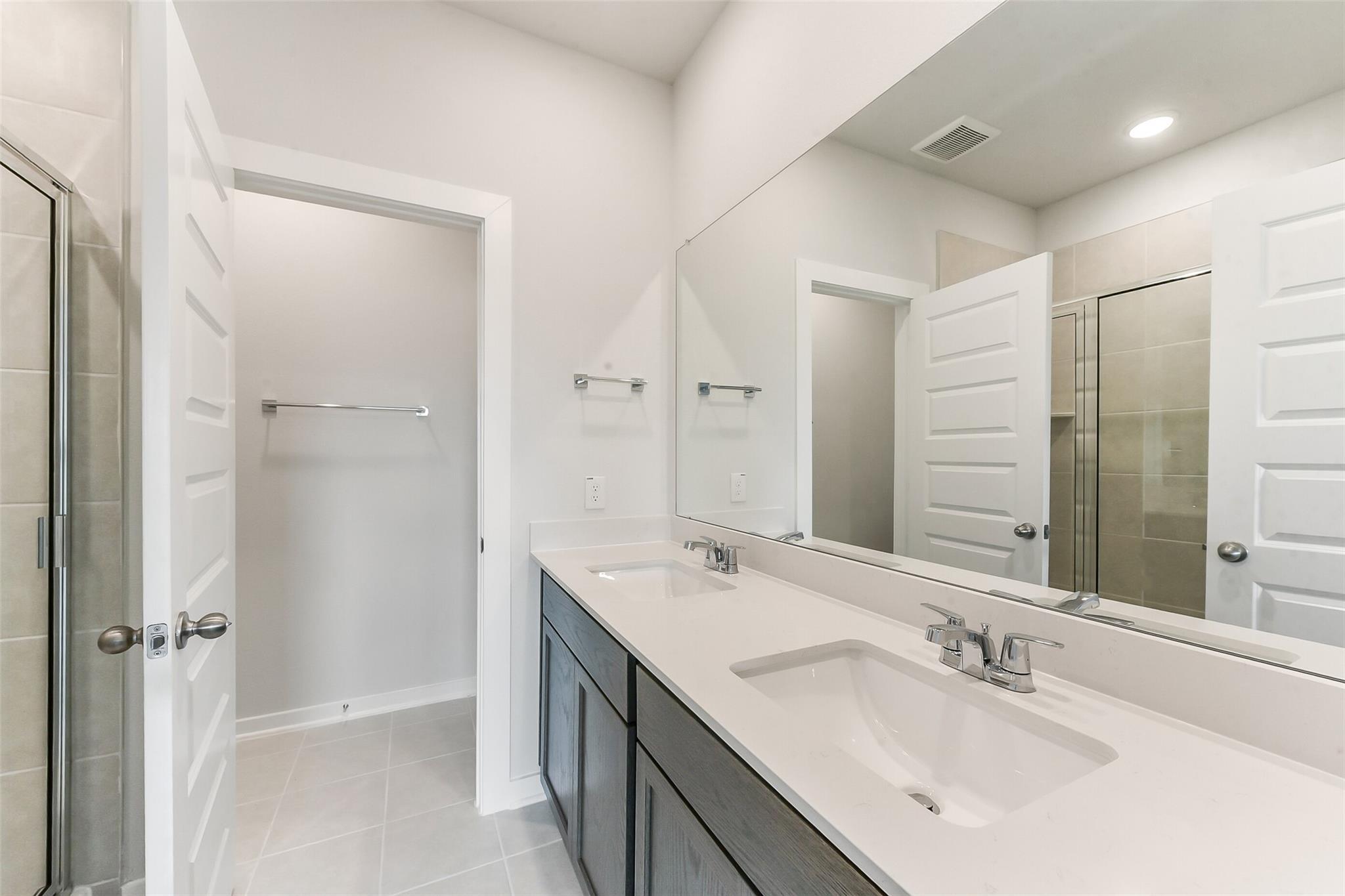 Elegant master bathroom with double quartz vanity, large mirror, frameless shower in Davidson Homes Sabine F, Dayton Texas