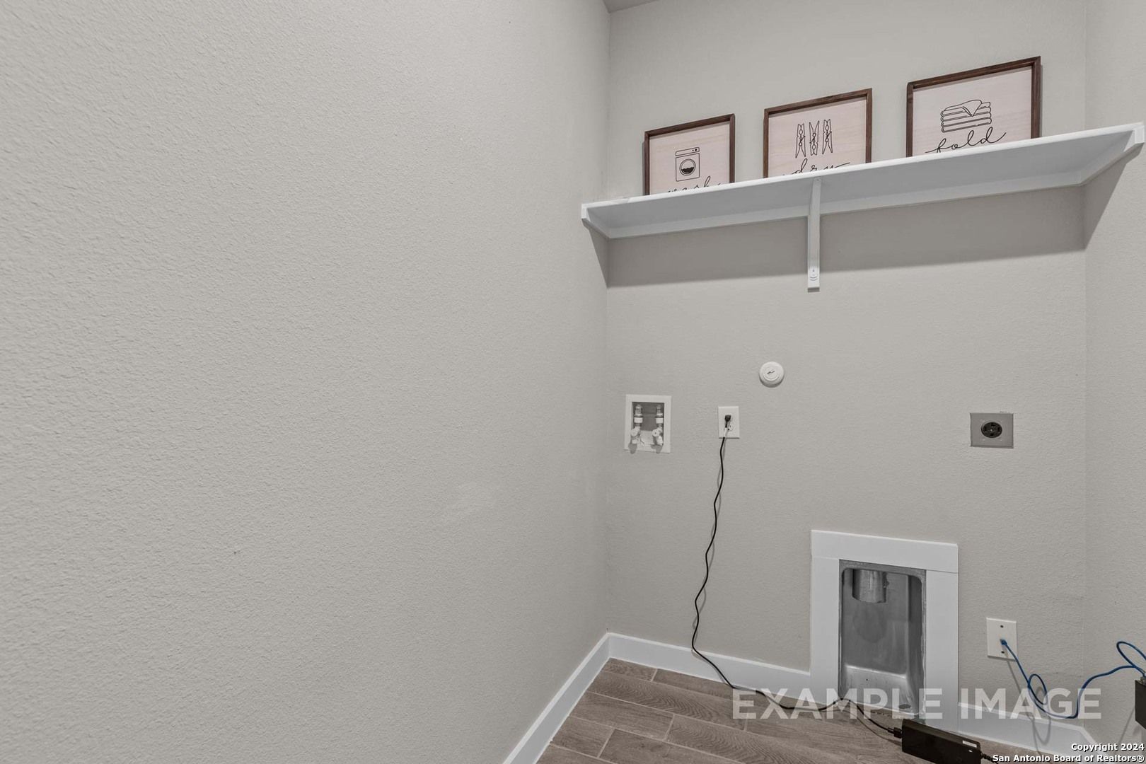 Modern laundry room with washer/dryer hookups, floating shelf, framed artwork, and tile flooring in Davidson Homes The Collin A, Seguin, Texas