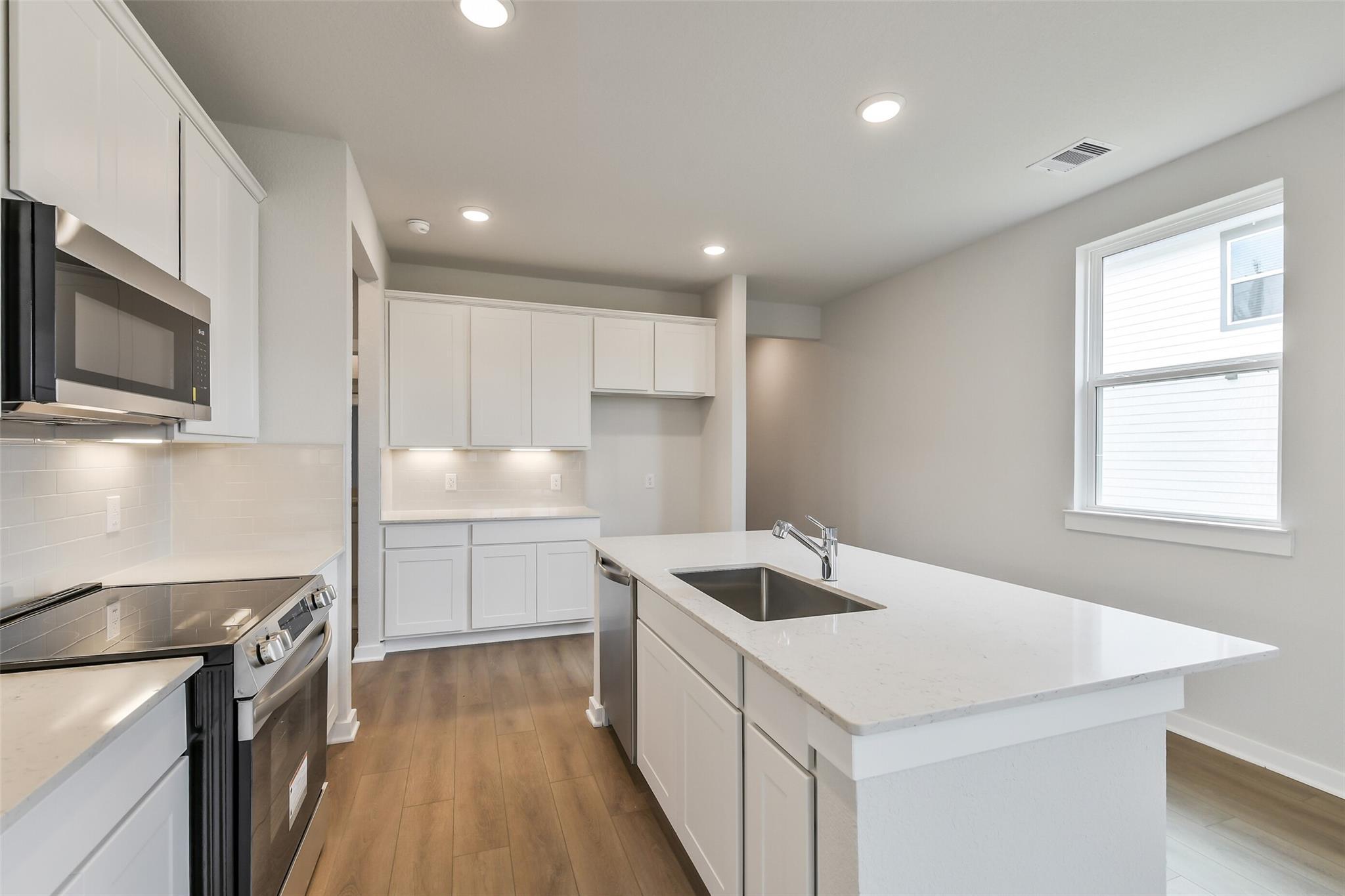 Modern open-concept kitchen with white cabinets, stainless appliances, and quartz island in Davidson Homes The Frio G, Cleveland, TX