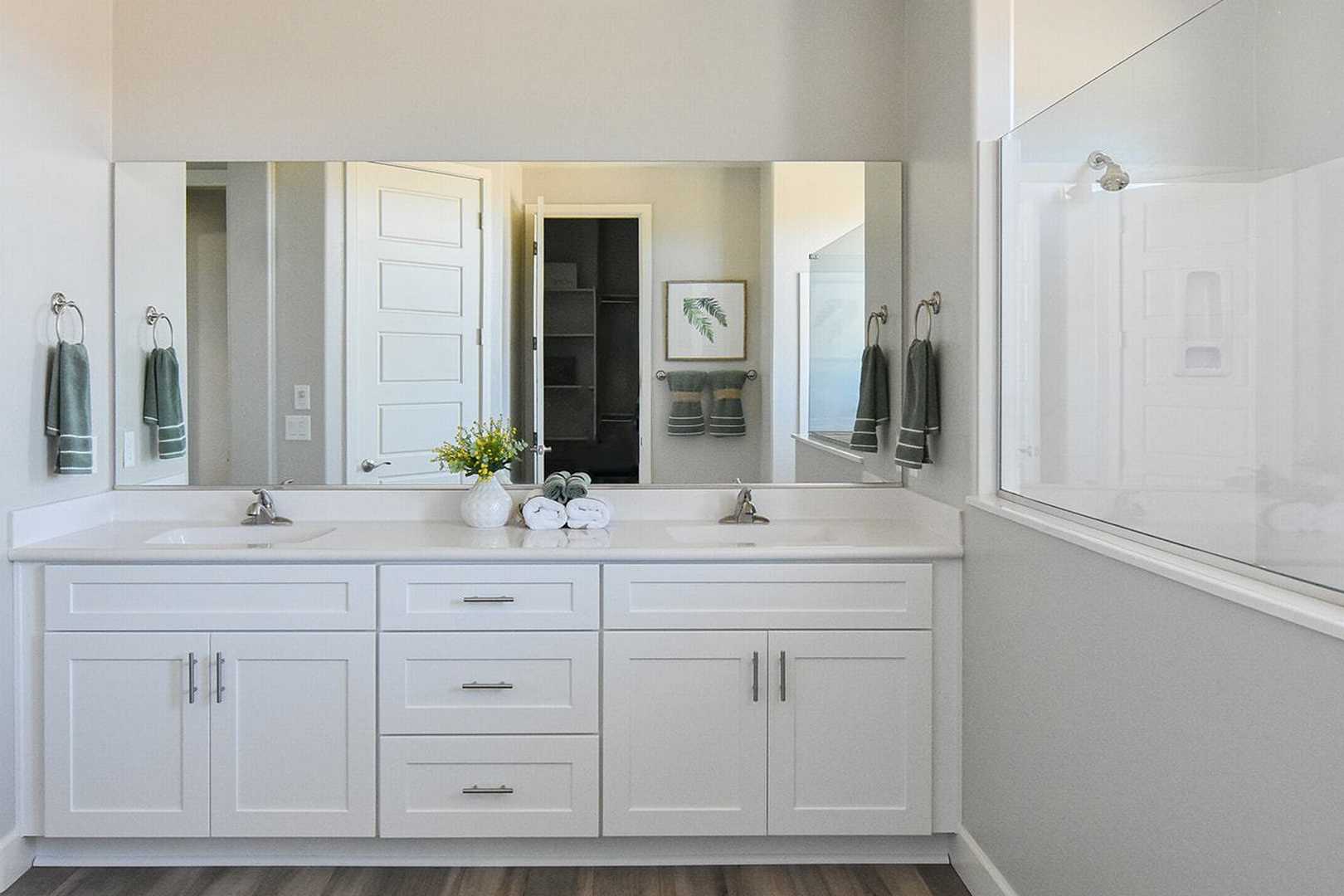 Spacious master bathroom in The Summit B with white double vanity, frameless mirrors, glass walk-in shower, and neutral tones