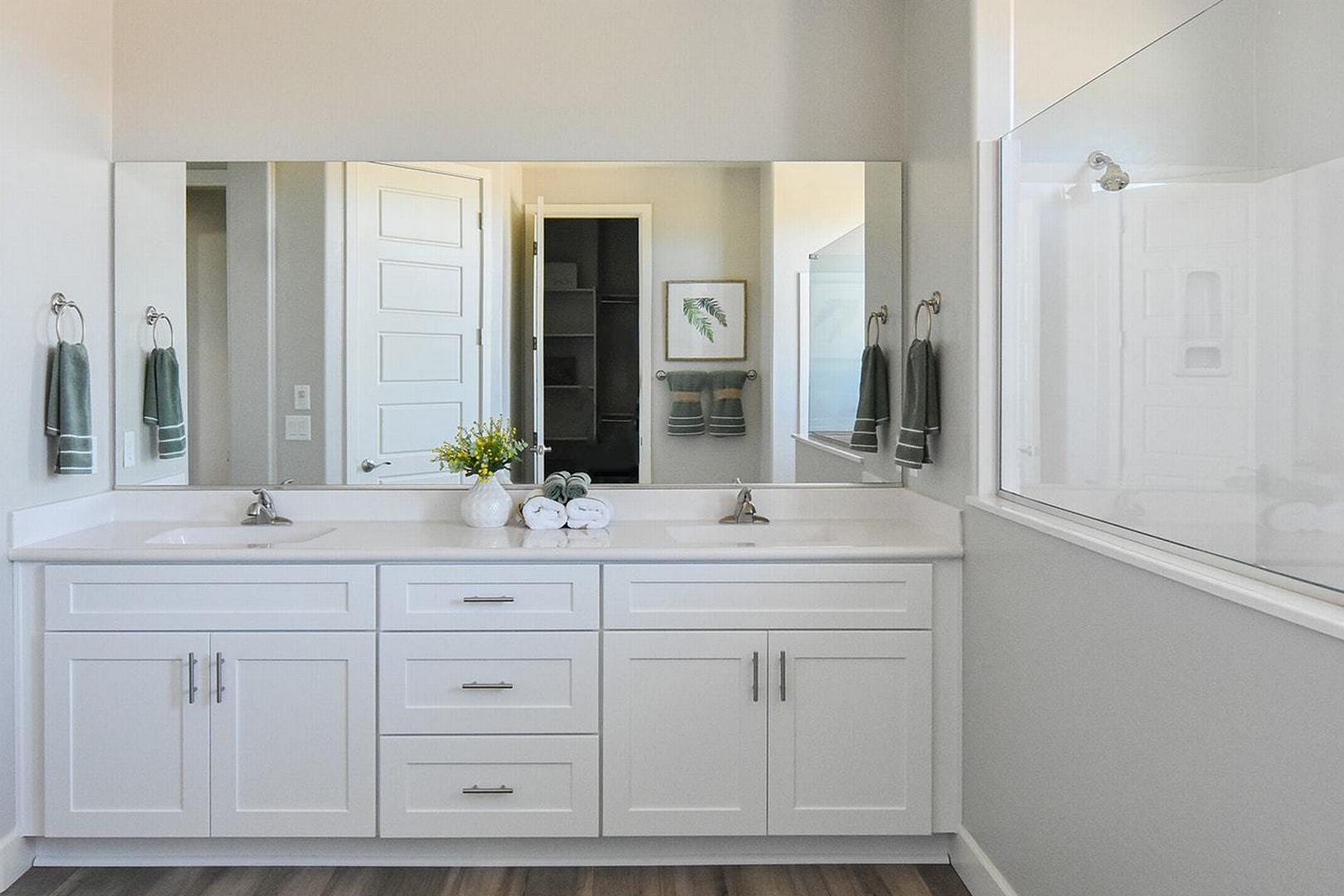 Spacious master bathroom in The Summit E with white double vanity, green towels, and frameless glass shower