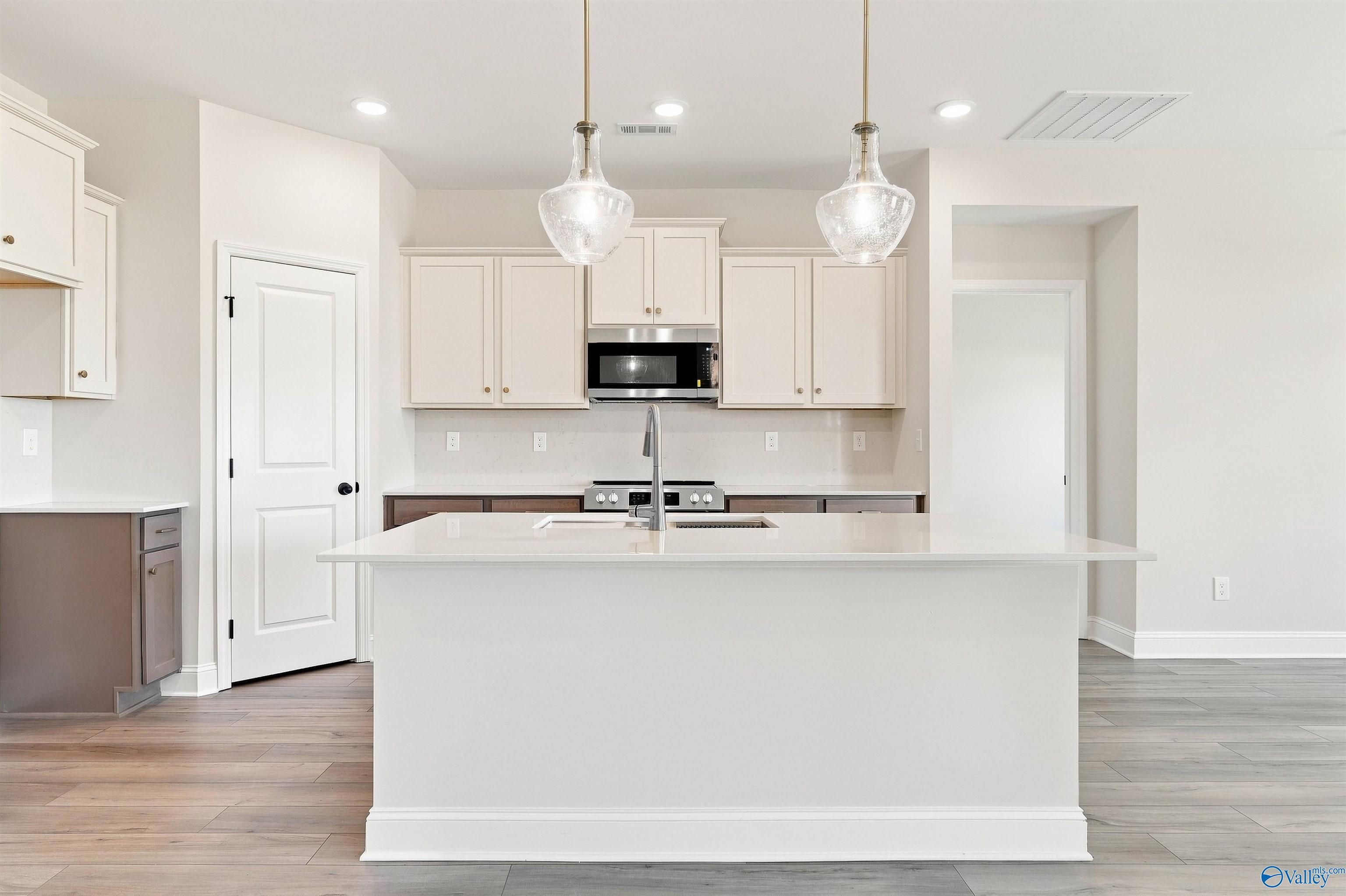 Large white kitchen island with pendant lights, cream cabinets, and stainless appliances in Davidson Homes Everett B, Toney, AL
