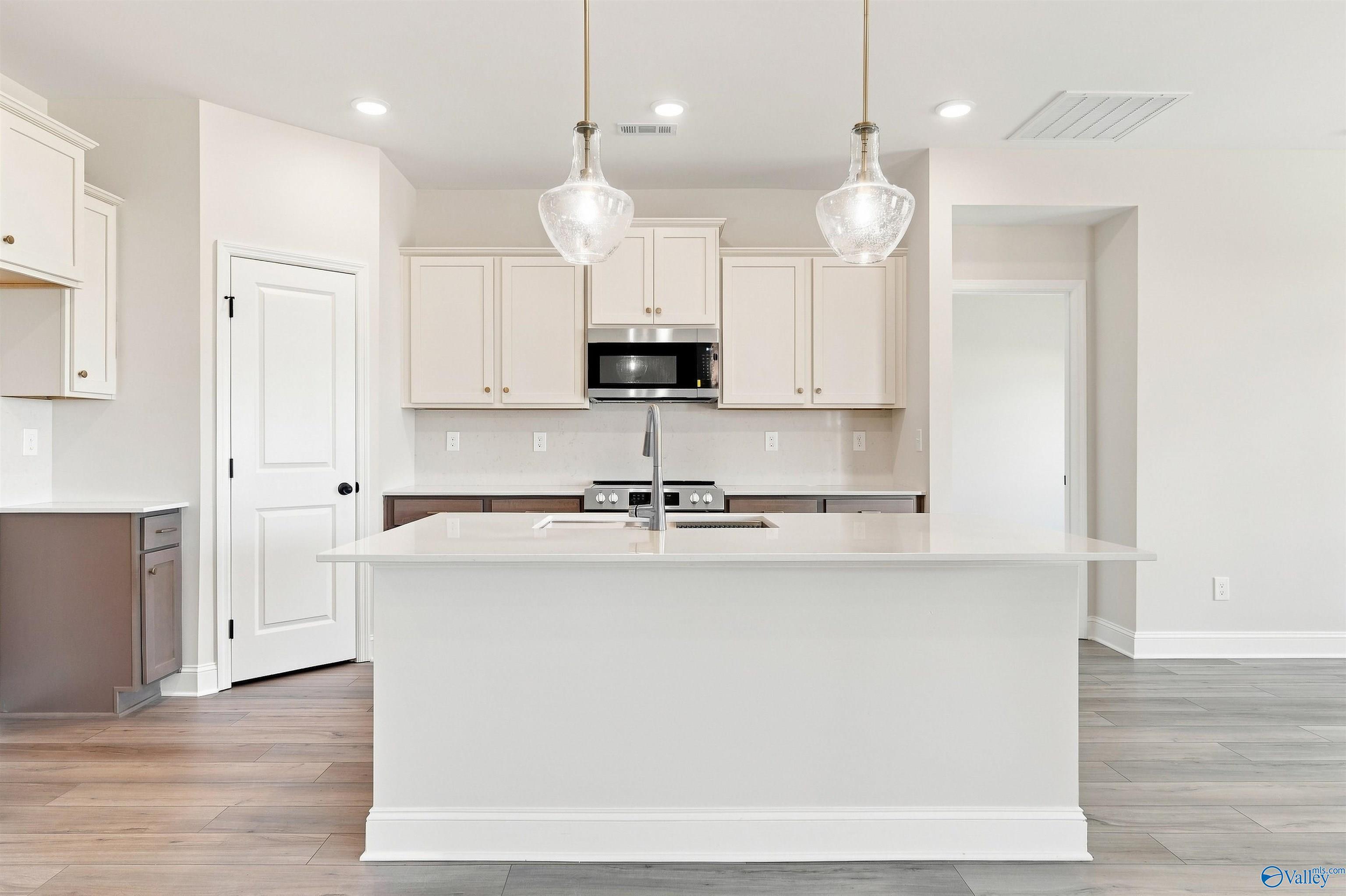 Large white kitchen island with pendant lights, cream cabinets, and stainless appliances in Davidson Homes Everett B, Toney, AL