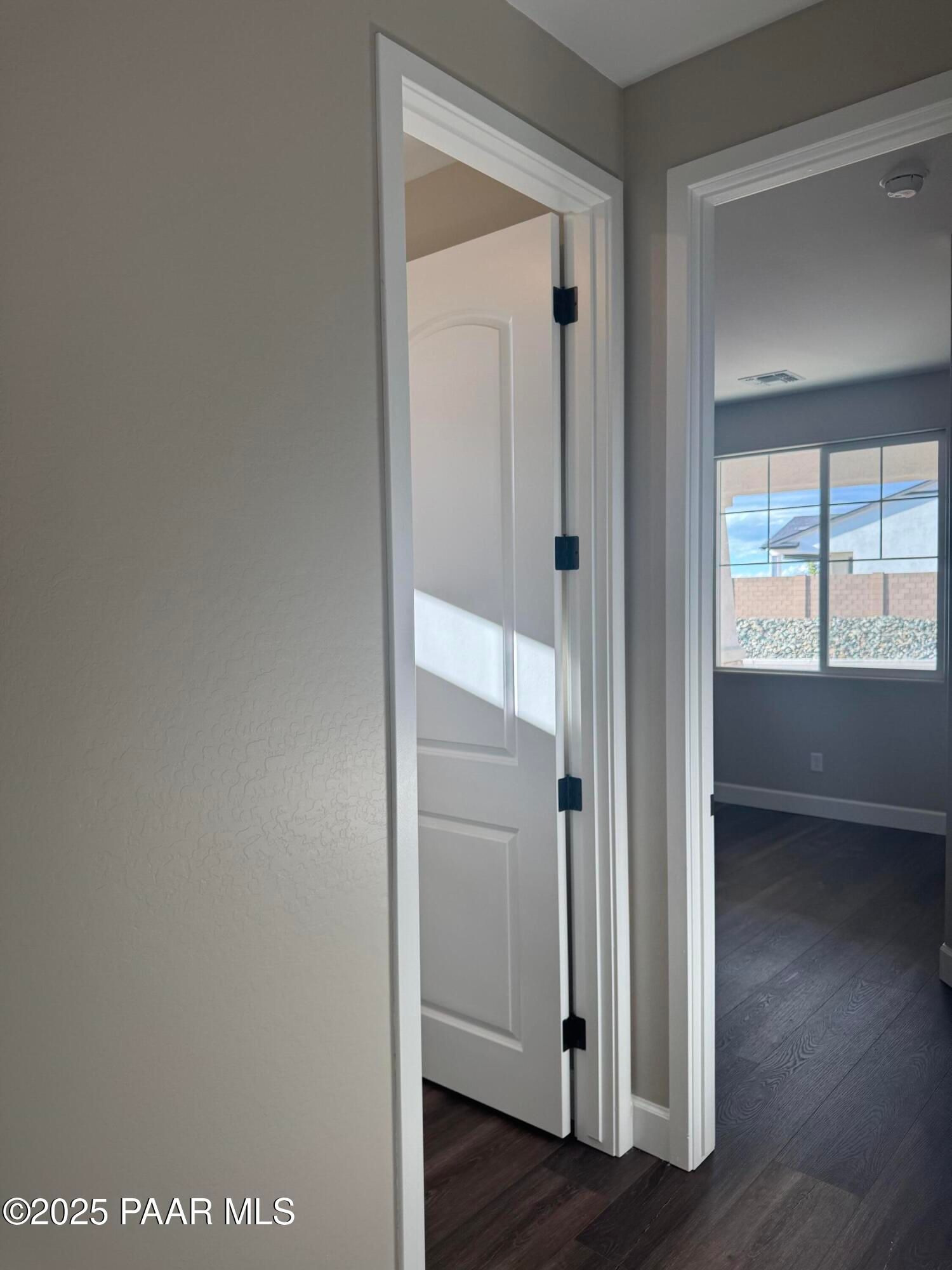 Bright hallway with open white doors, hardwood floors, and sunlit window in Evermore Homes The Sunrise A, Prescott Valley, Arizona