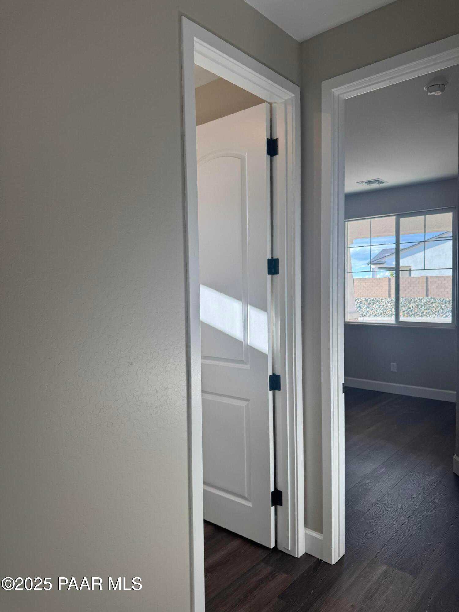 Bright hallway with open white doors, hardwood floors, and sunlit window in Evermore Homes The Sunrise A, Prescott Valley, Arizona