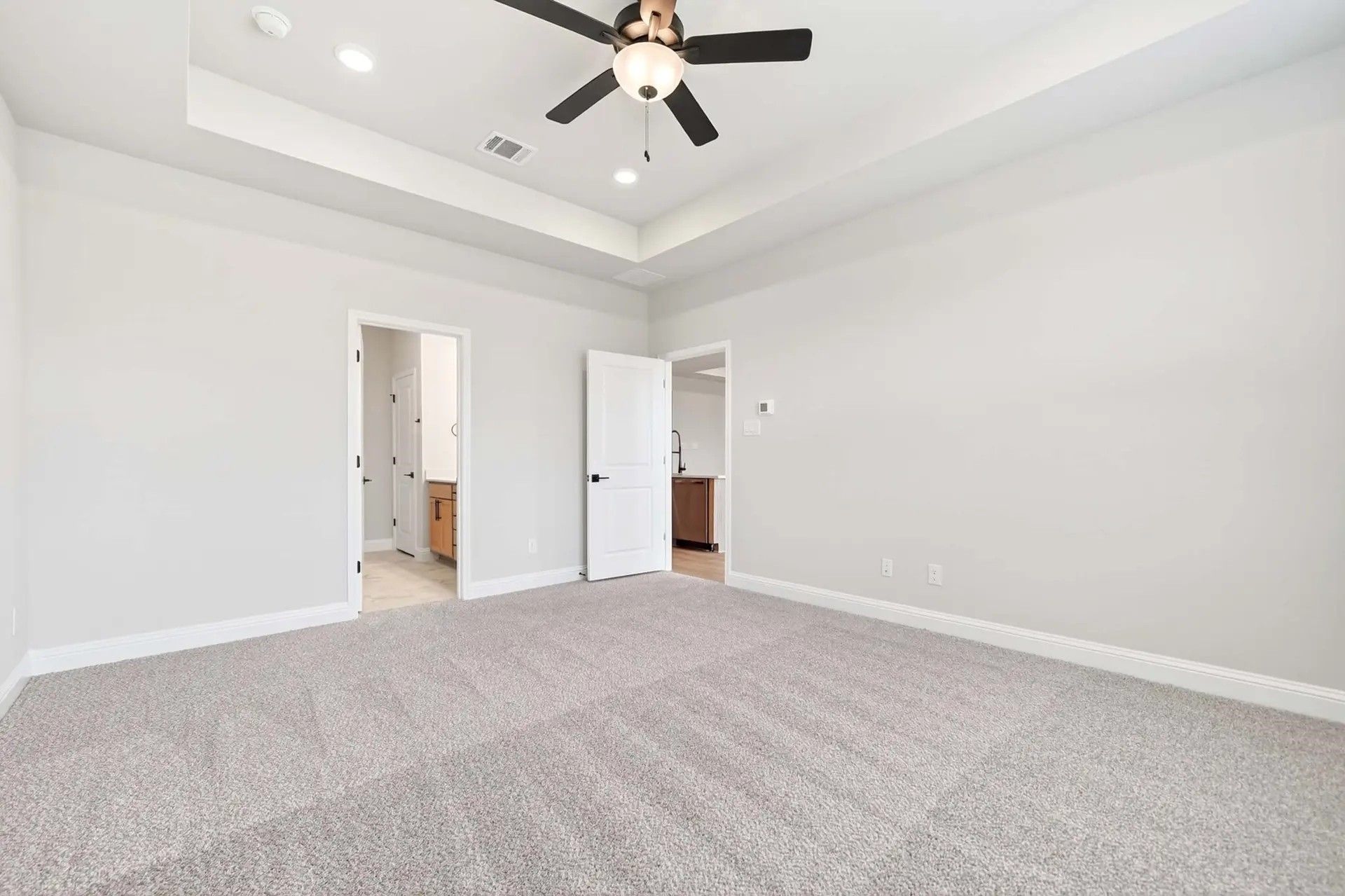 Spacious bedroom with tray ceiling and ceiling fan in The Holly C floor plan by Davidson Homes in Heartland, Texas.