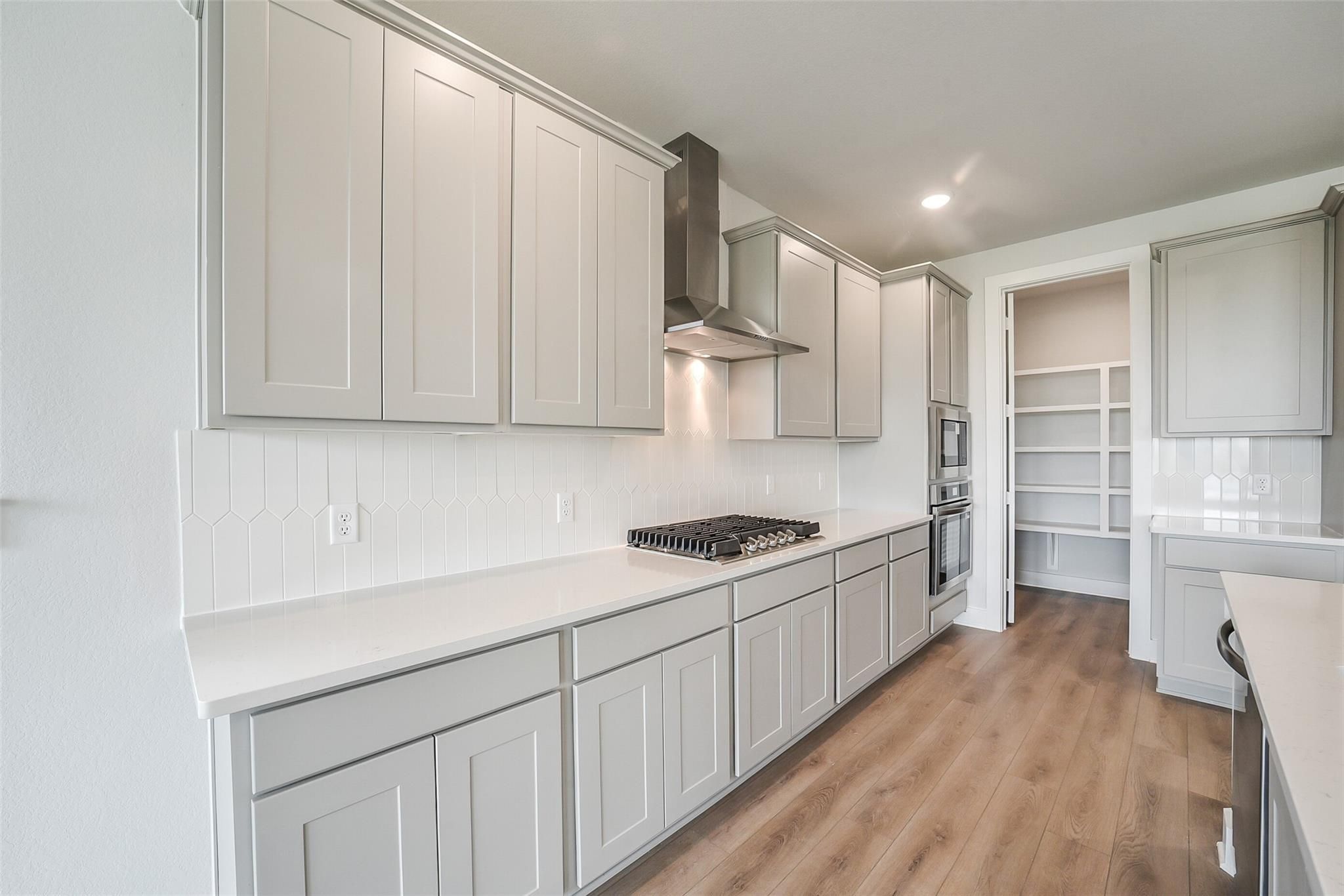 Modern white kitchen with shaker cabinets, stainless steel range, subway tile backsplash, and quartz counters in Davidson Homes The Philip B, Rosharon, TX