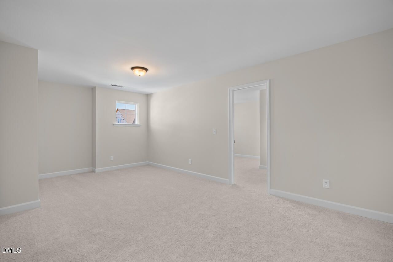 Spacious empty bedroom with beige walls, plush carpet, and window in Davidson Homes The Ashport M plan at Wendell Ridge, Wendell NC