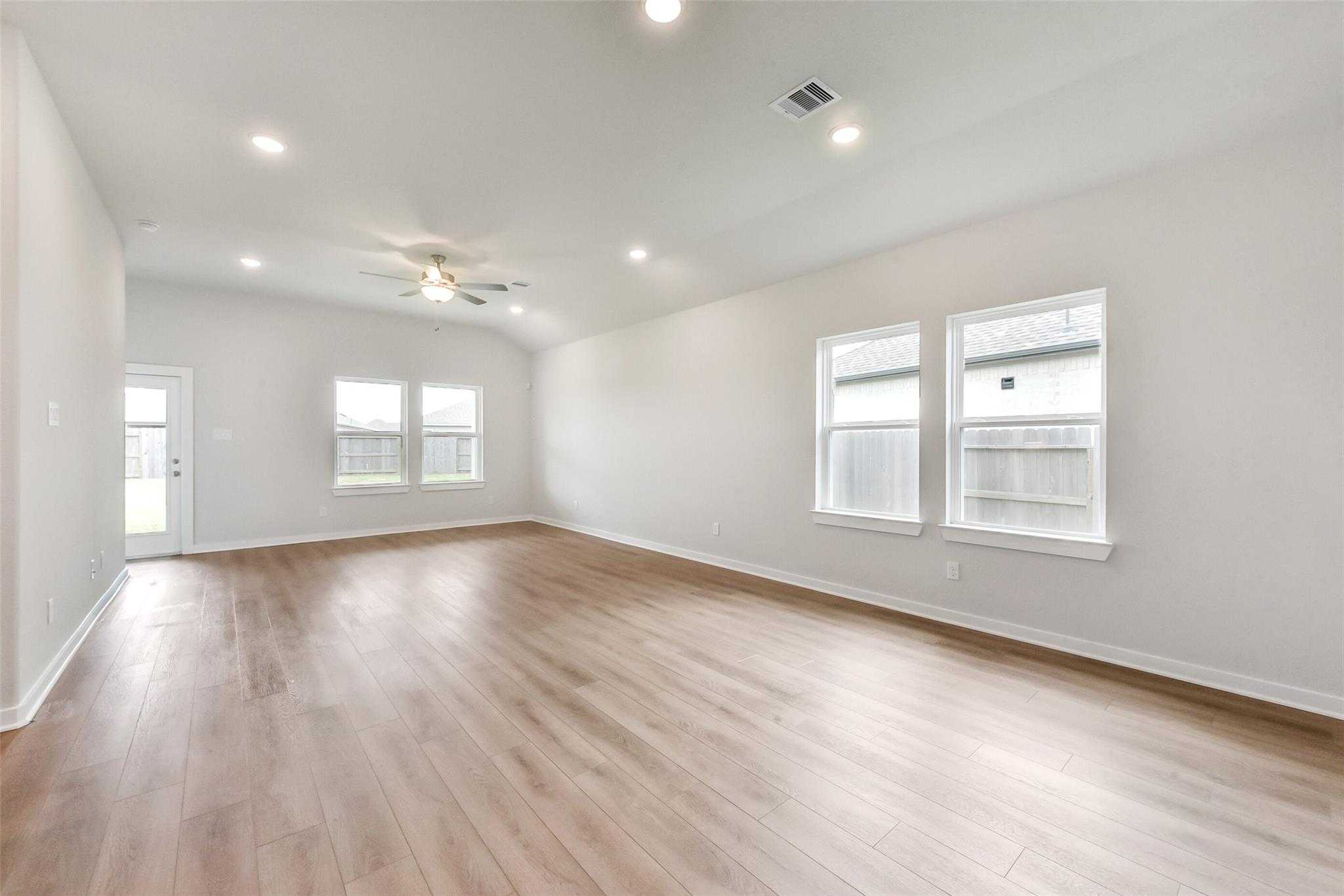 Spacious open living room with light hardwood floors, large windows, ceiling fan in Davidson Homes The Laguna C, Rosharon, Texas