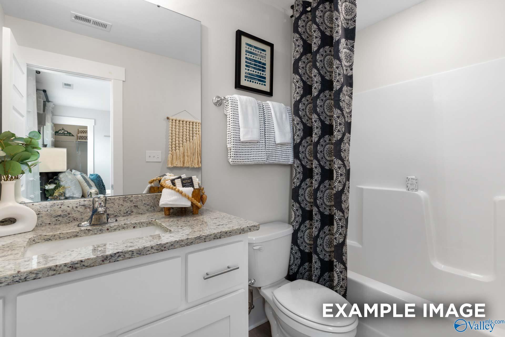 Bathroom with granite vanity countertop, white cabinets, and tub shower in Davidson Homes Chelsea A plan, Ivy Hills, Toney, Alabama