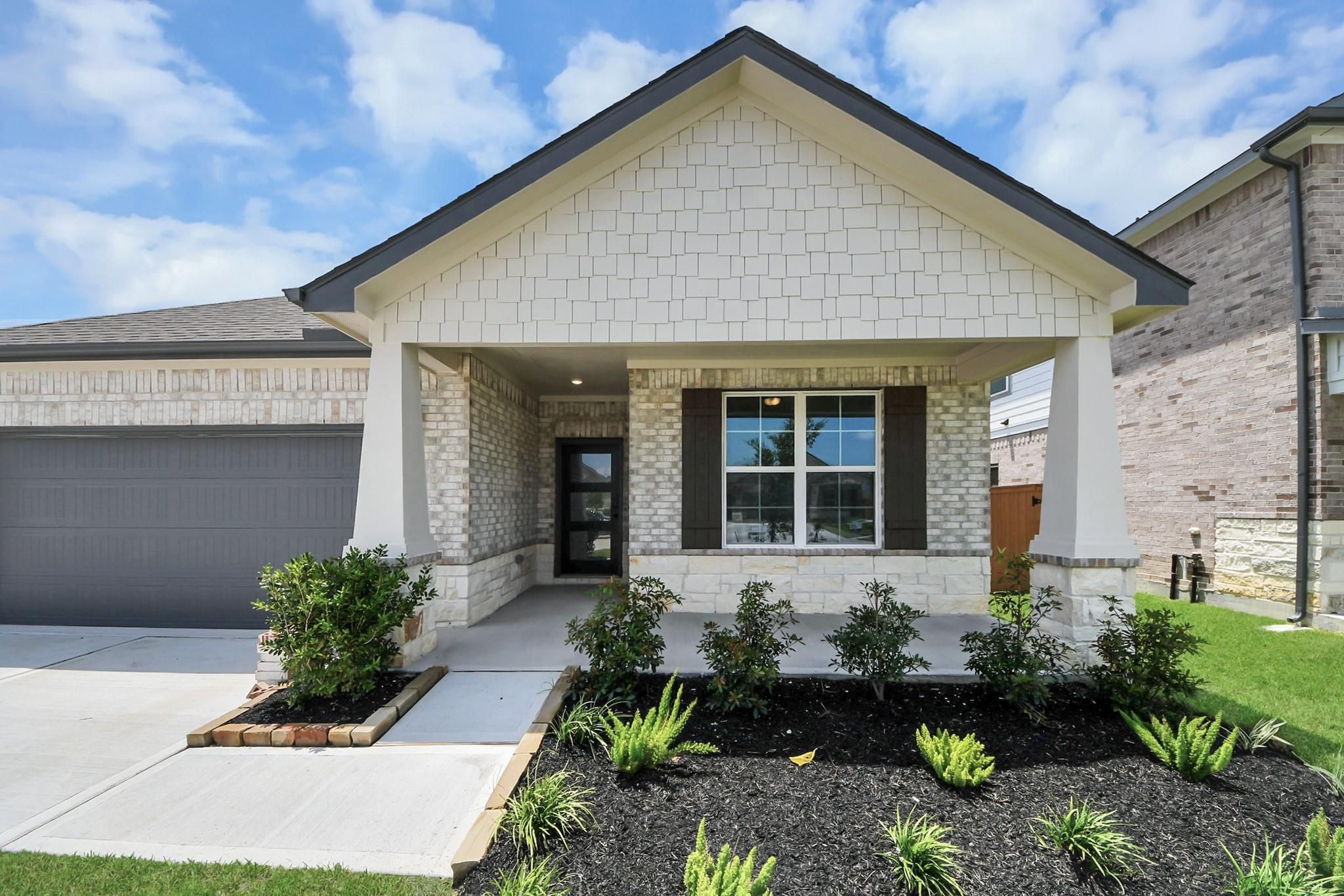 Brick and stone front exterior with covered porch and 3-car garage at The Everett C, Davidson Homes in River Ranch Meadows, Dayton, TX