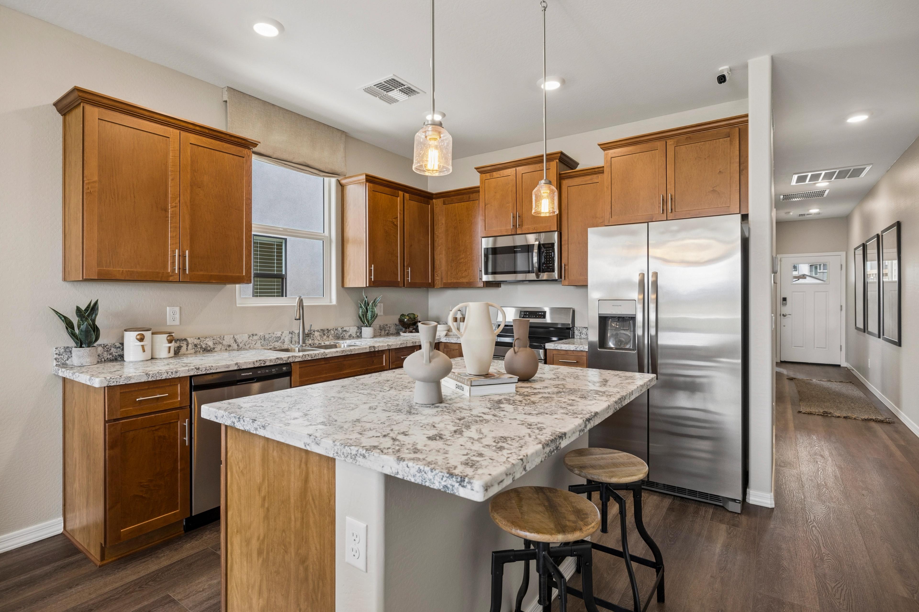 Modern kitchen with warm wood cabinets, quartz island, pendant lights, and stainless steel appliances at Senator Cottages in Prescott AZ