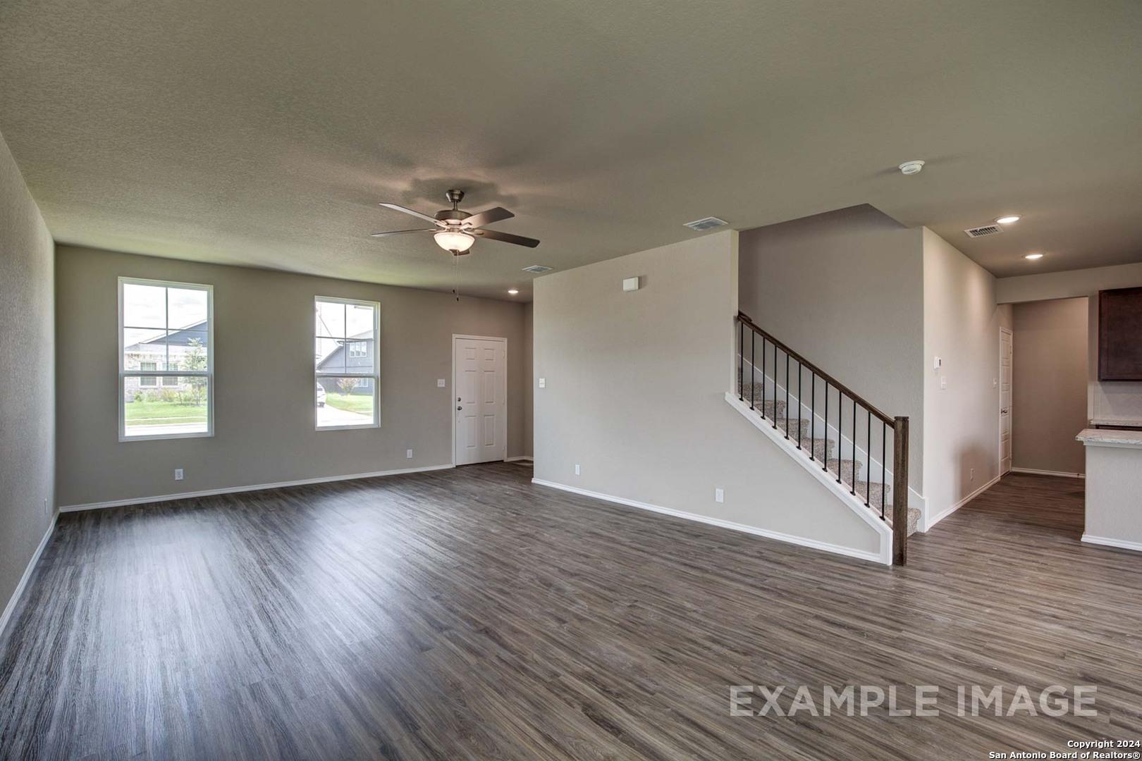 Spacious living area with hardwood floors, large windows, ceiling fan, and staircase in Davidson Homes The Murray J, Bricewood, San Antonio
