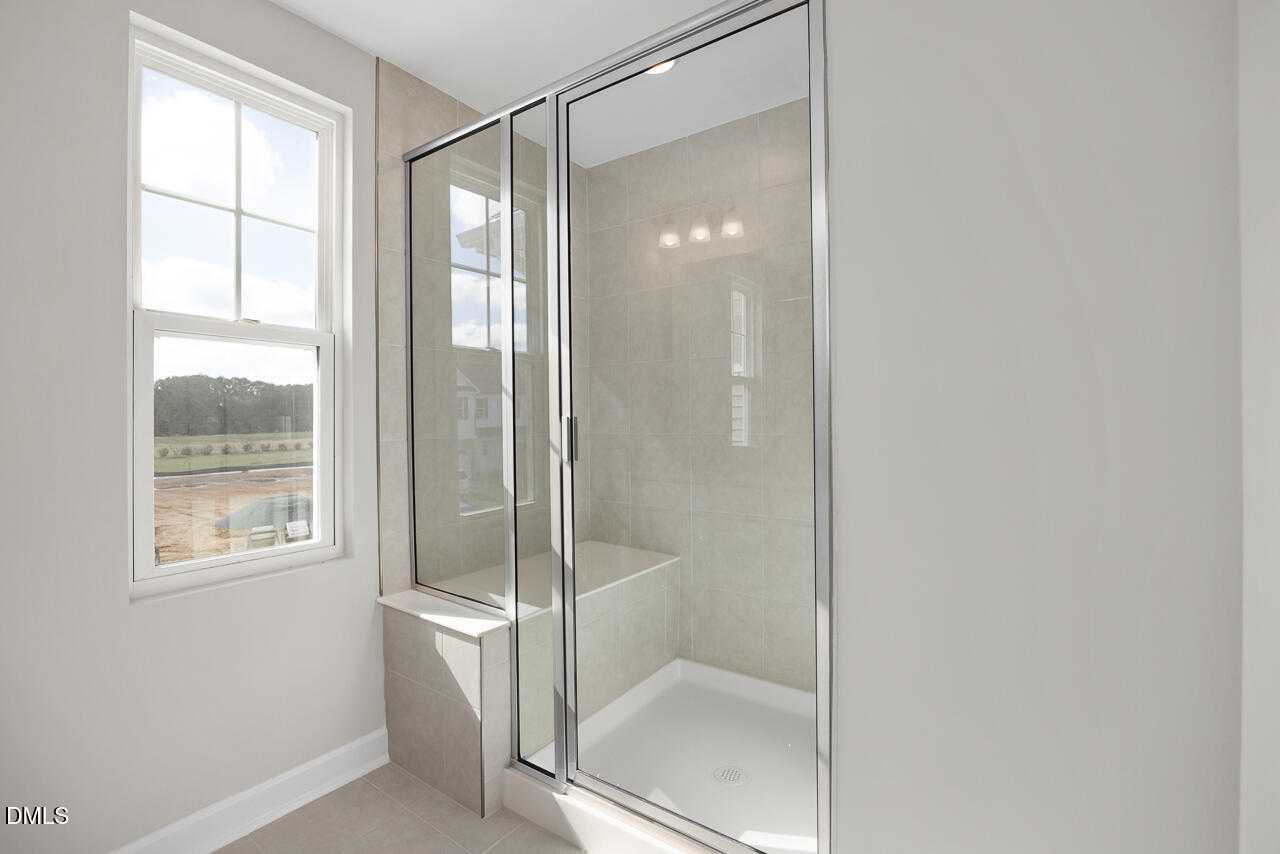 Spacious walk-in shower with frameless glass doors, tiled walls, bench seat, and natural light in master bath, Davidson Homes The Warren, Fuquay-Varina, NC