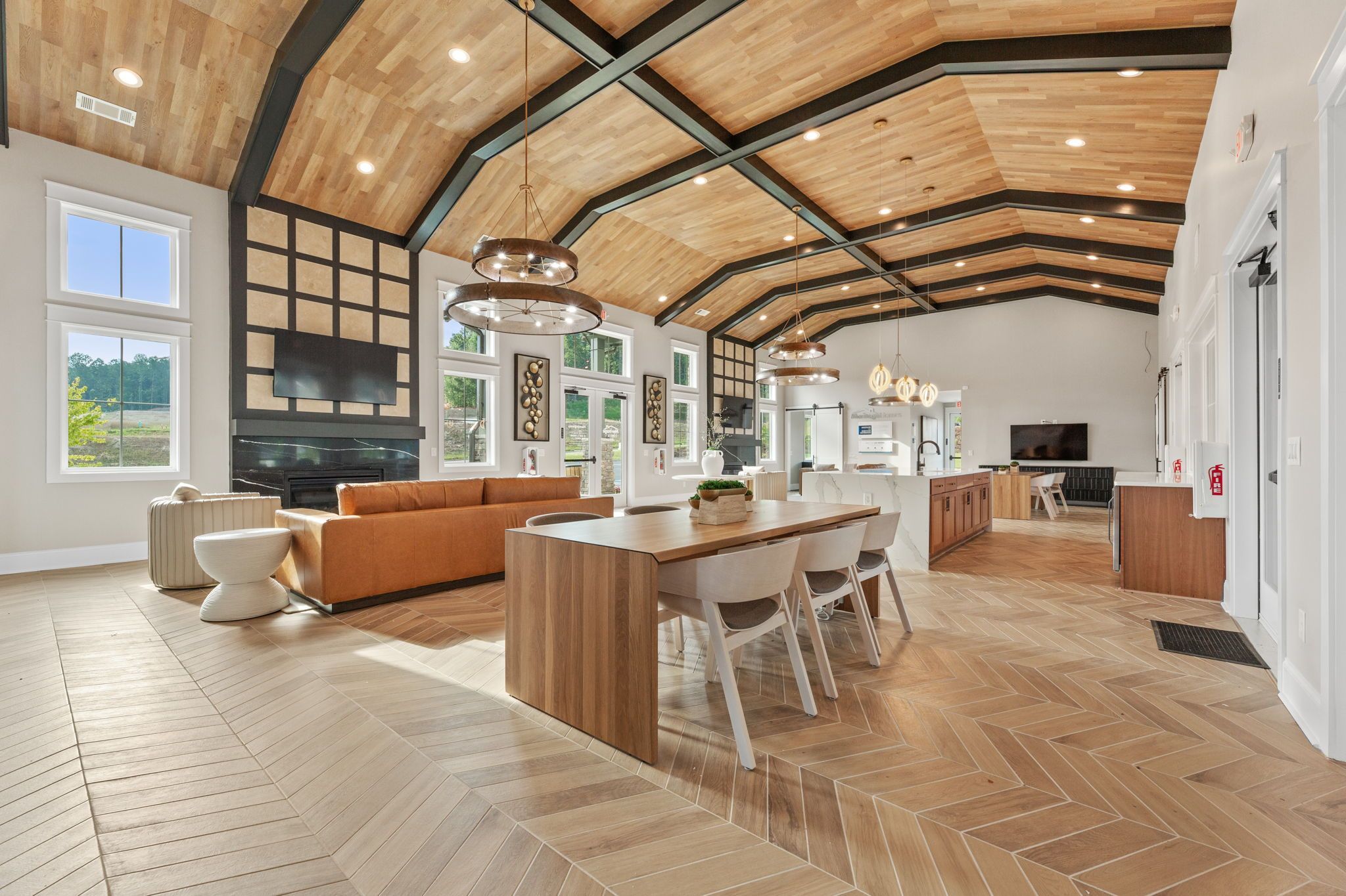 Spacious clubhouse interior at Hemingway in Cumming GA with beamed wooden ceiling, modern kitchen island, orange sofa, fireplace, and herringbone floors