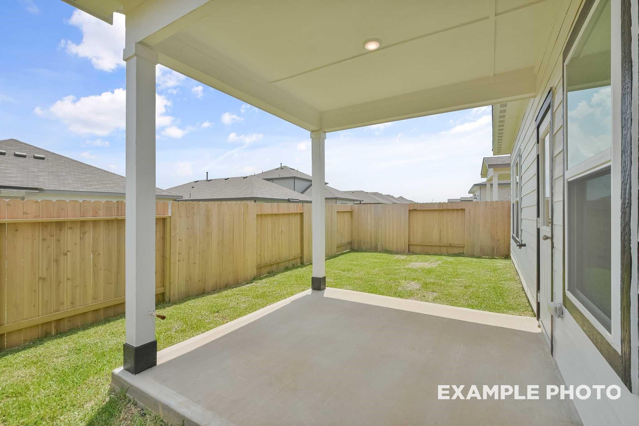 Covered back patio with white posts, wooden fence, and green lawn in Davidson Homes The Frio F, Conroe, Texas