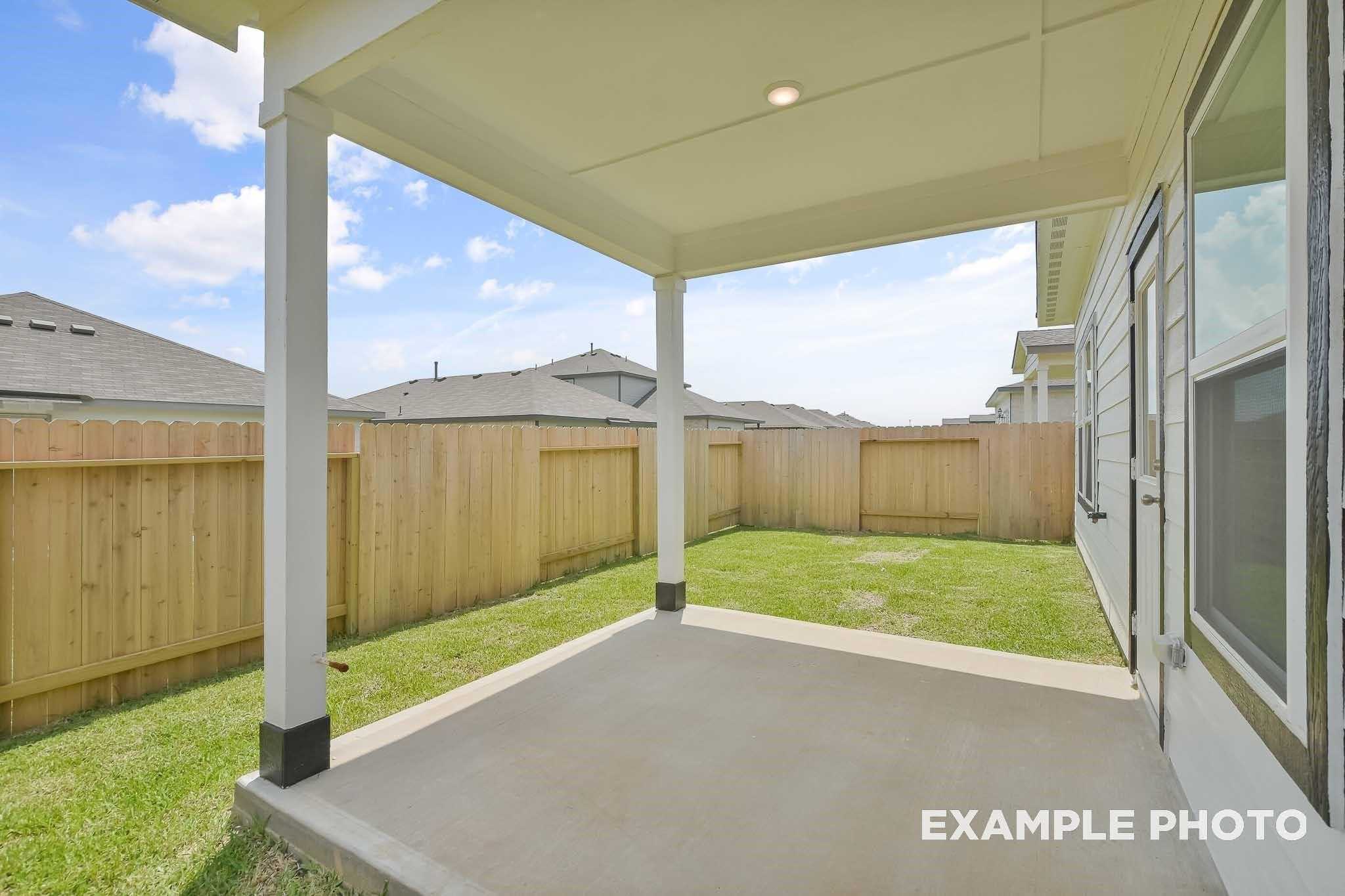Covered back patio with white posts, wooden fence, and green lawn in Davidson Homes The Frio F, Conroe, Texas