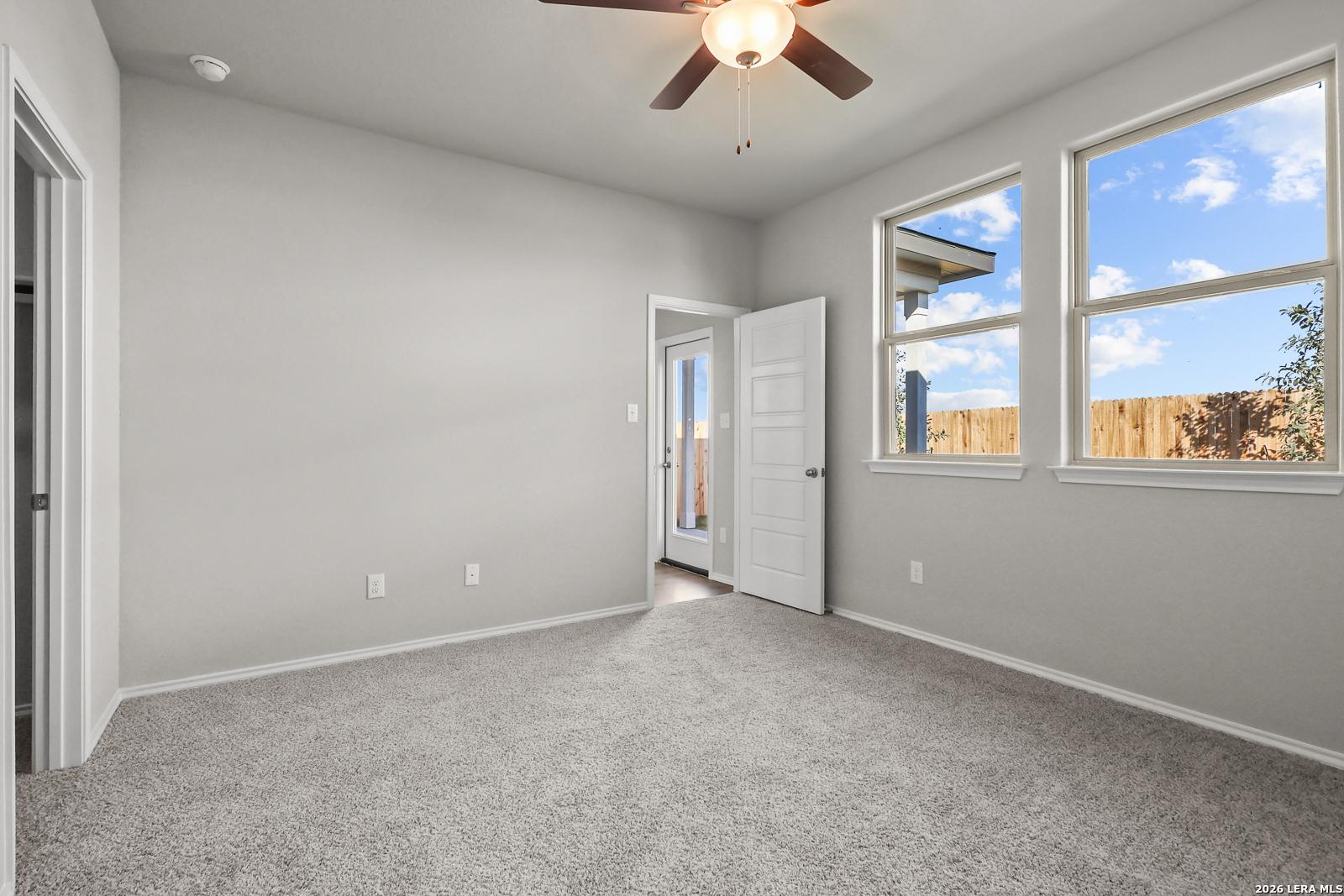 Bright secondary bedroom with gray walls, beige carpet, ceiling fan, and windows overlooking backyard in Davidson Homes The Frio B, San Antonio